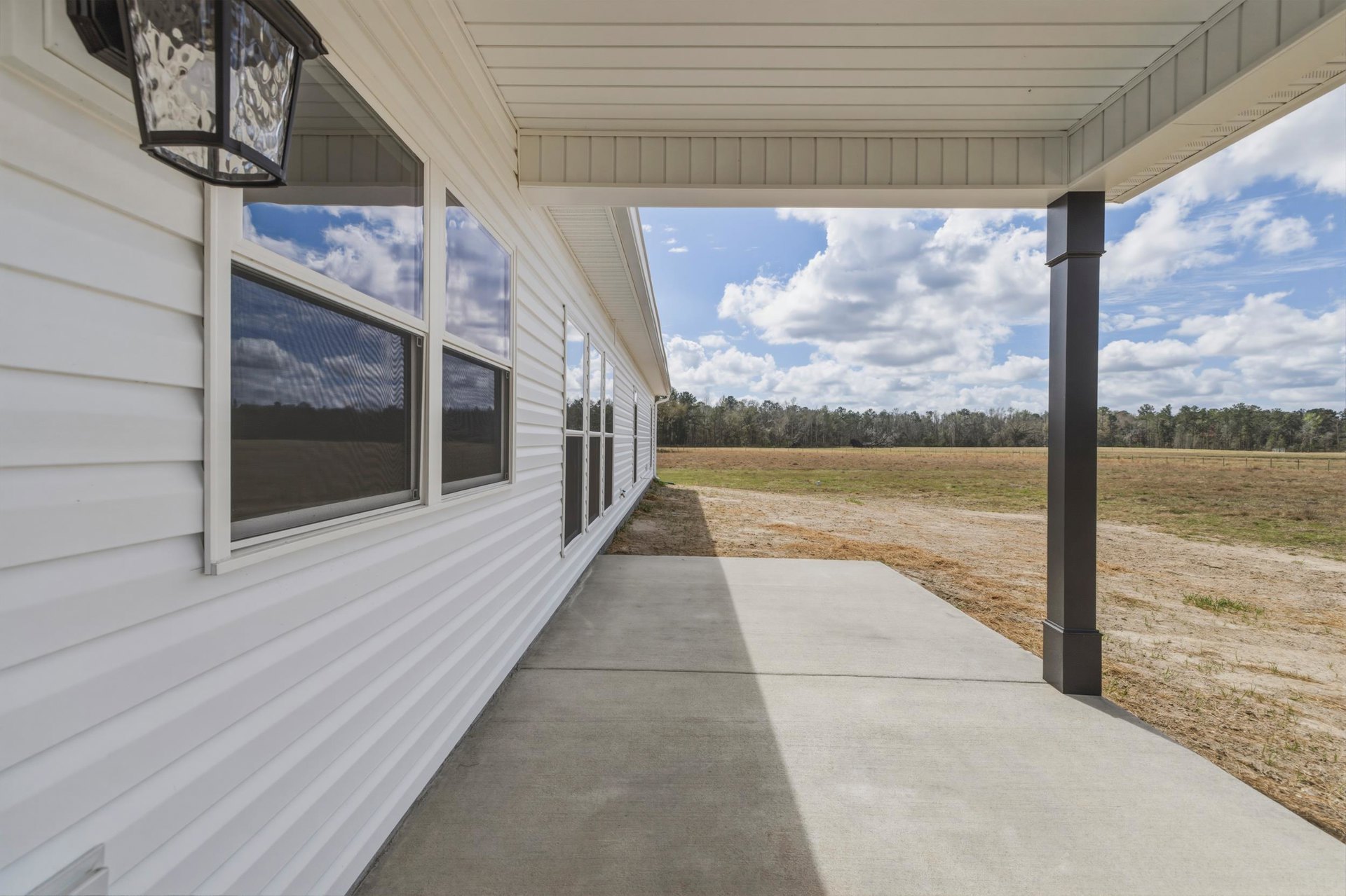 White siding house with large windows, concrete walkway, green grass lawn, and blue sky with scattered clouds