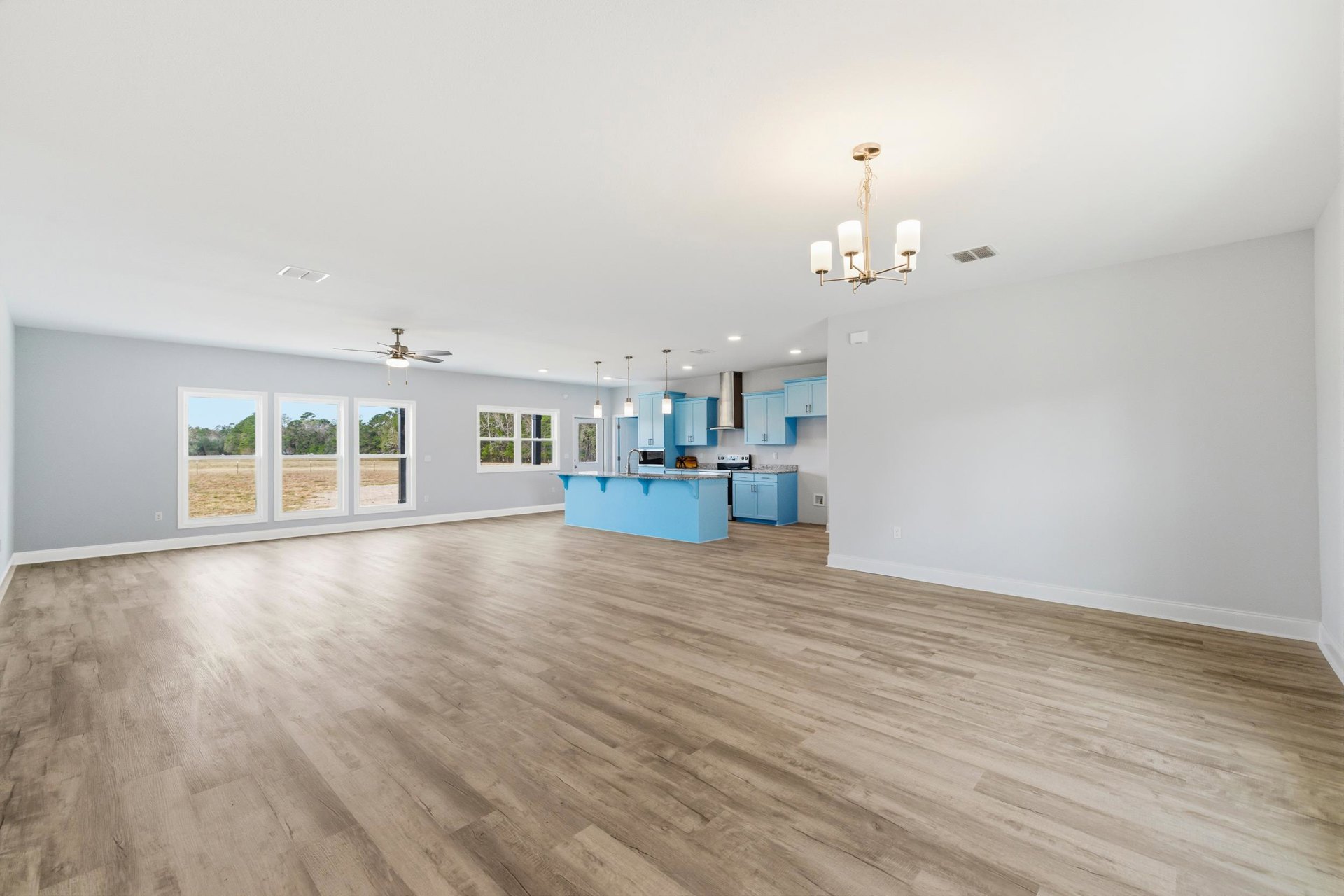 Spacious room with wood flooring, blue cabinets, marble countertop, row of windows overlooking trees, lamp on a table, and blue accent wall