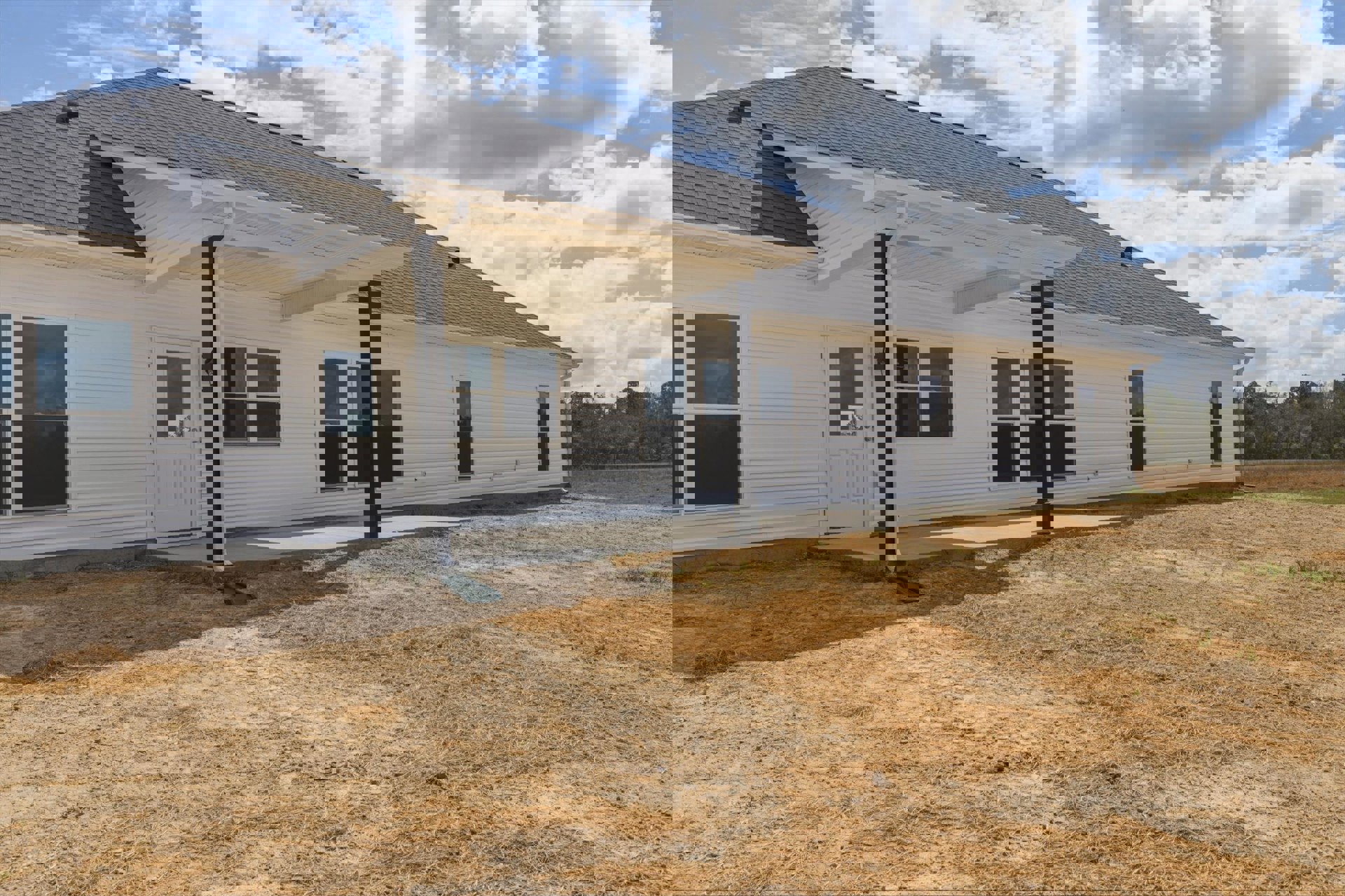 White house with black-framed windows, covered front porch, expansive green yard, and playground set in foreground under partly cloudy sky