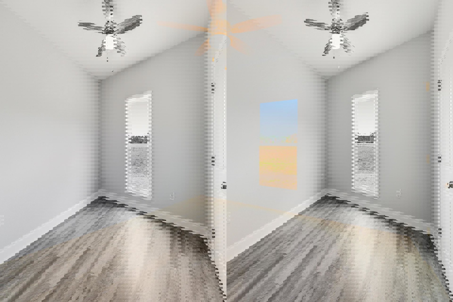 Bedroom with wood flooring, white plaster walls, large window overlooking grassy field, ceiling fan with integrated light fixture