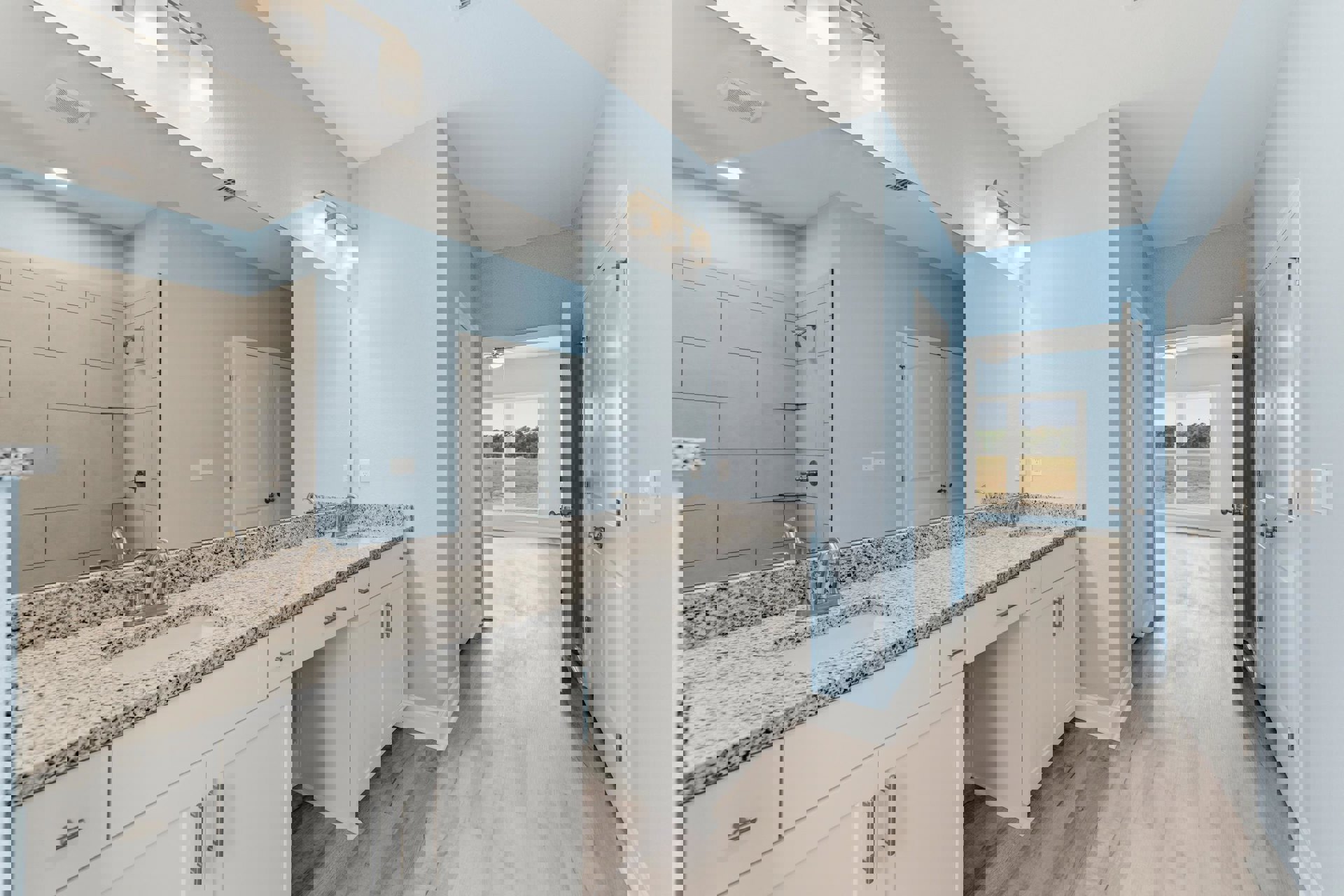 Bathroom with marble countertop, double sinks, large wall mirror, light fixture above, tiled floor, cabinetry, and window overlooking a field.