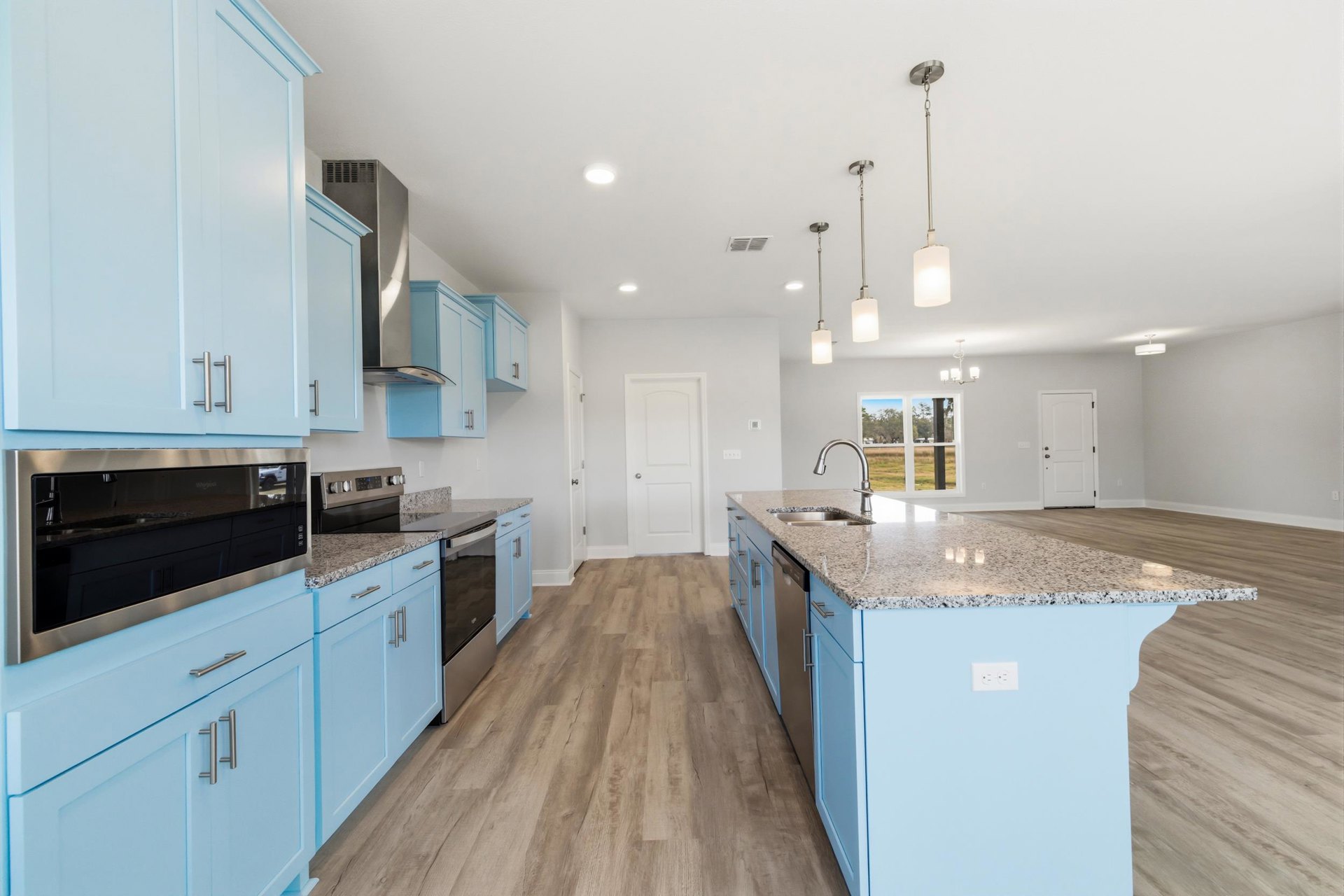 Blue kitchen cabinets with silver handles, marble countertop, stainless steel oven, kitchen island with integrated sink, white doors with contrasting handles, light wood flooring
