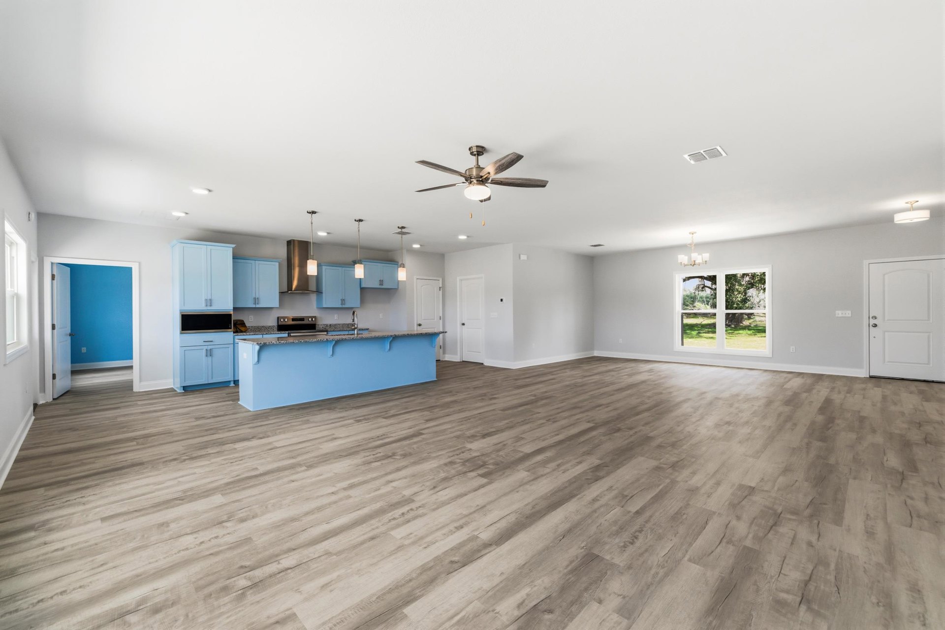 Open-concept kitchen with blue cabinetry, white countertop island, wood laminate flooring, ceiling fan with light, blue accent wall, and white doors with silver handles