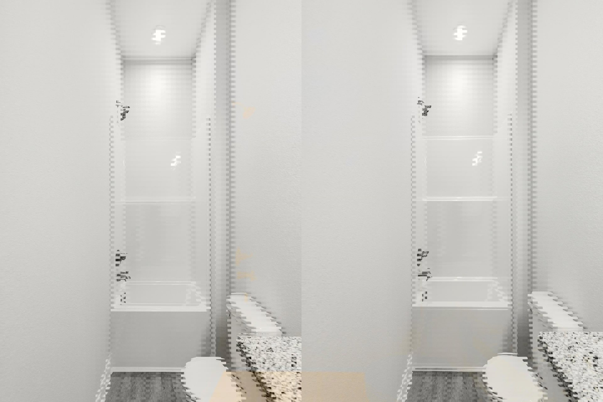 White bathtub with chrome shower head, adjacent toilet with closed lid, light gray tile flooring, white countertop with built-in sink, recessed ceiling light, smooth plaster walls.