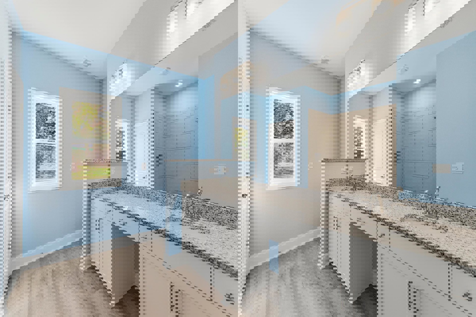 Bathroom with marble countertop, rectangular mirror above sink, tile shower wall, white door with silver handle, window overlooking trees.