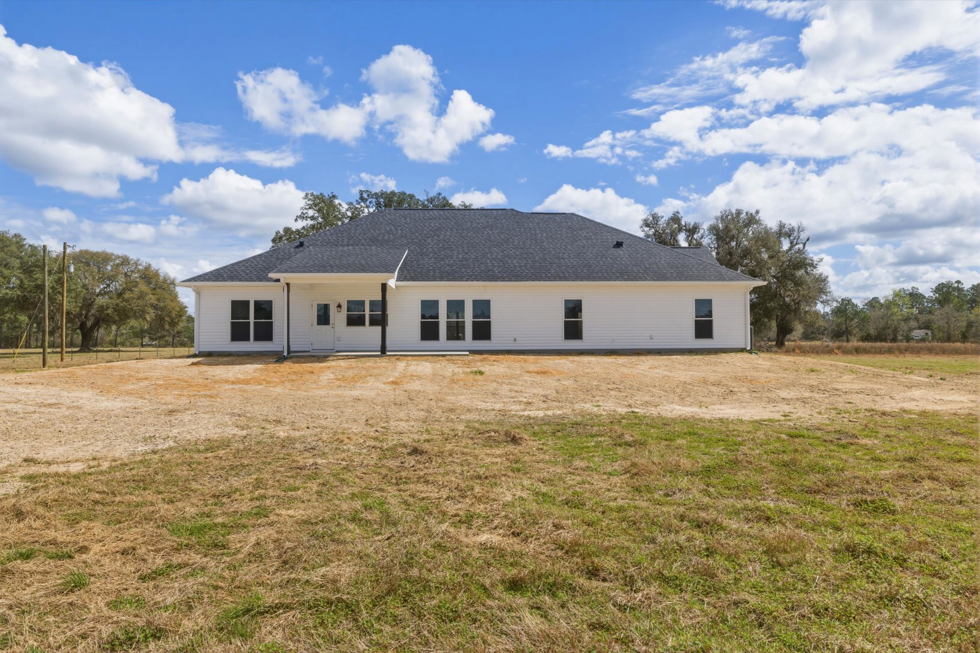 White siding house with gabled roof, large grassy yard, mature trees in background, close-up window visible on side.