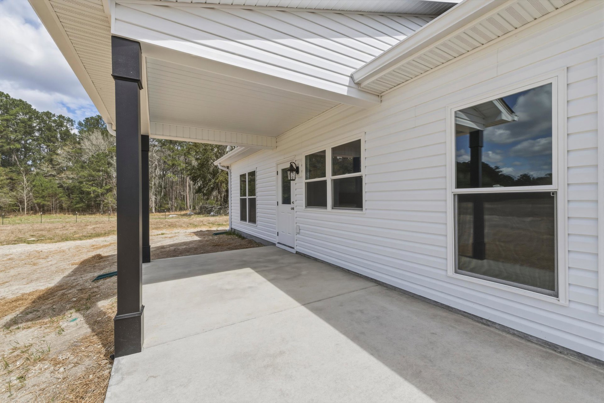 White siding house with covered front porch, white framed windows, shaded entry, and trees in background