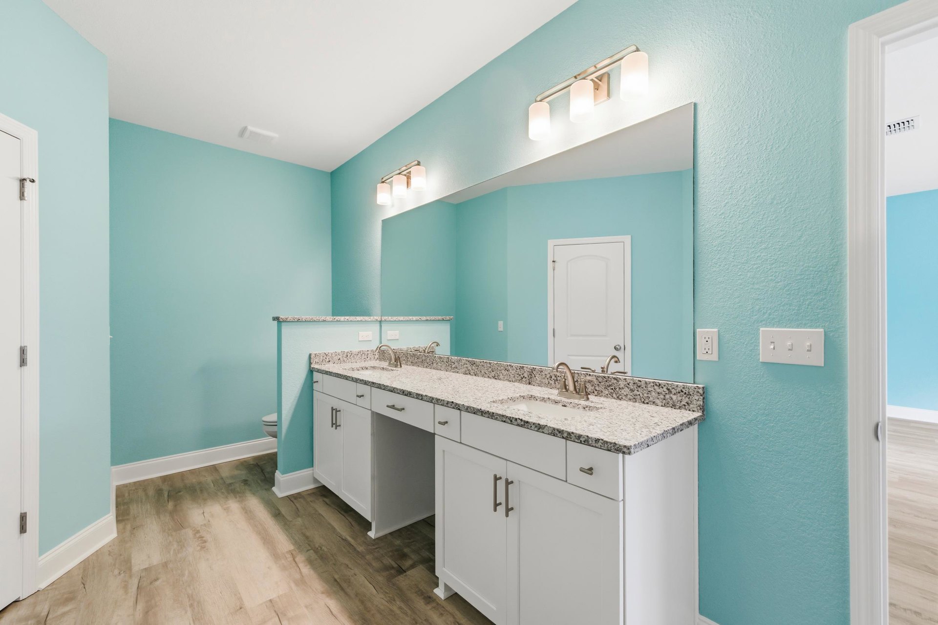 Bathroom with blue painted walls, white shaker-style cabinets, white door with silver handle, row of light switches, white rectangular wall light, tile flooring, and visible door