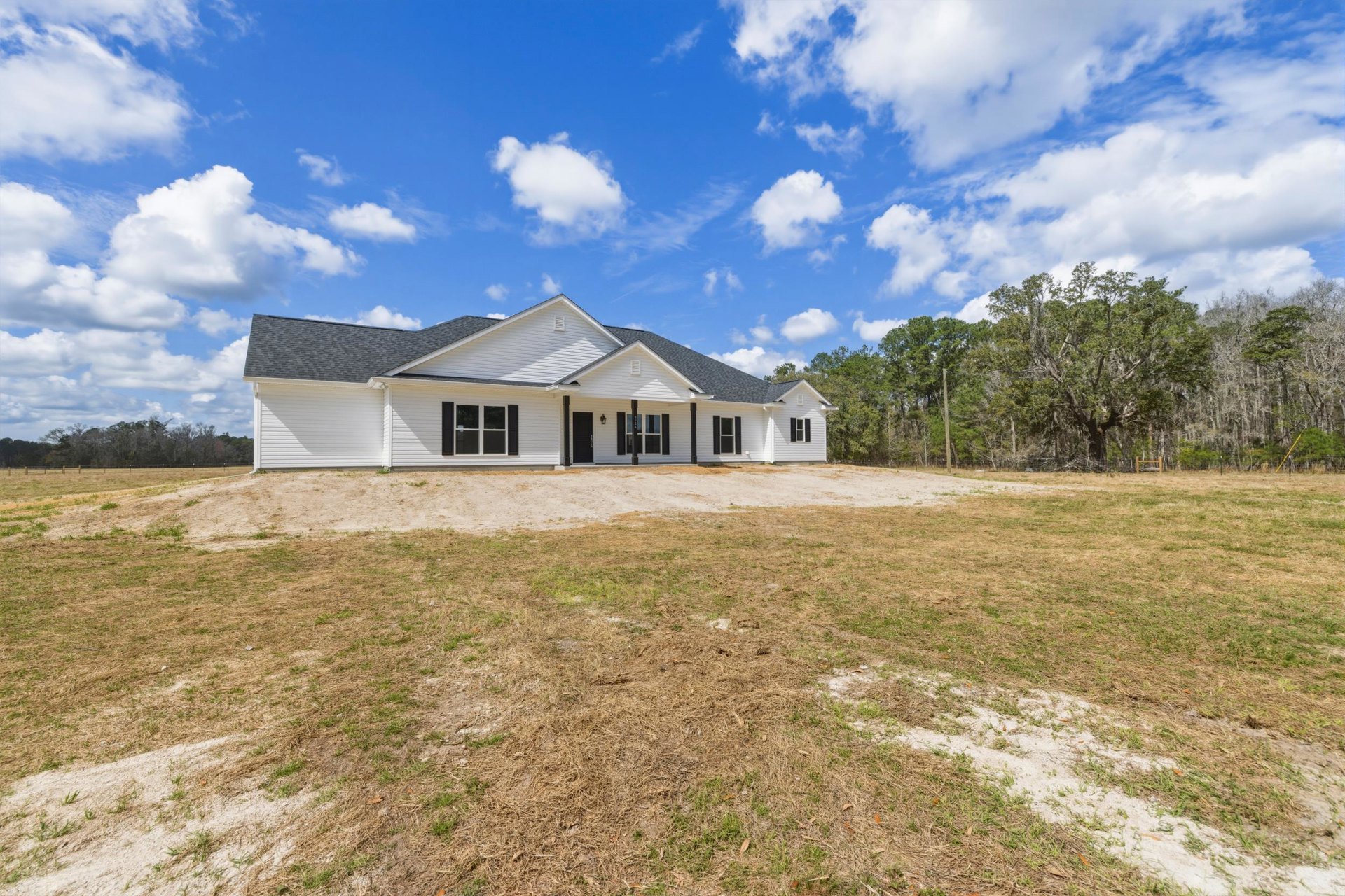 White house with black shutters, expansive grassy yard, large mature tree, blue sky, and white-framed windows
