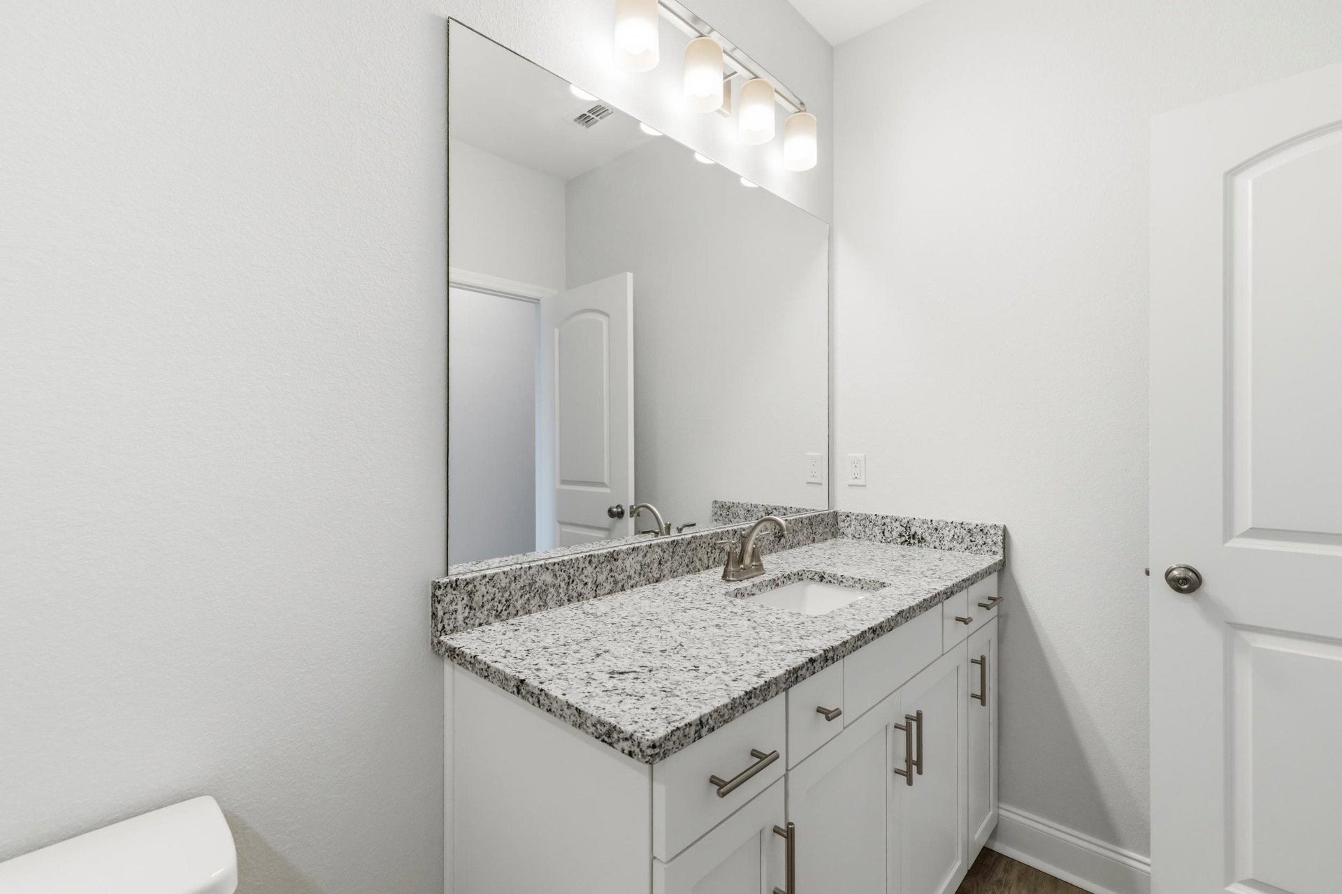 Bathroom with marble countertop, rectangular mirror above sink, chrome faucet, white cabinetry, and light tile walls