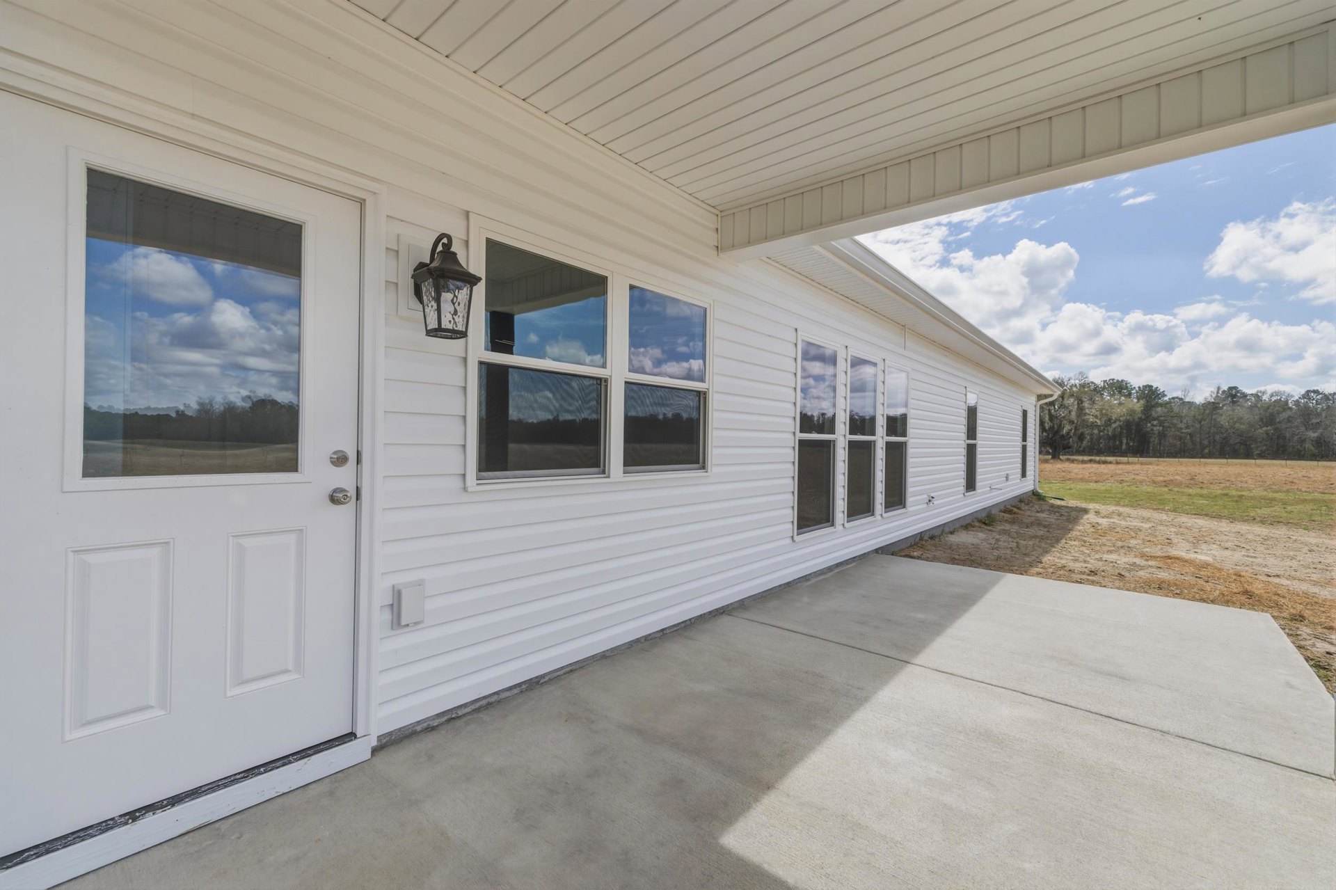 White siding home with covered porch, white front door, large windows reflecting blue sky, and black metal light fixture near entry.