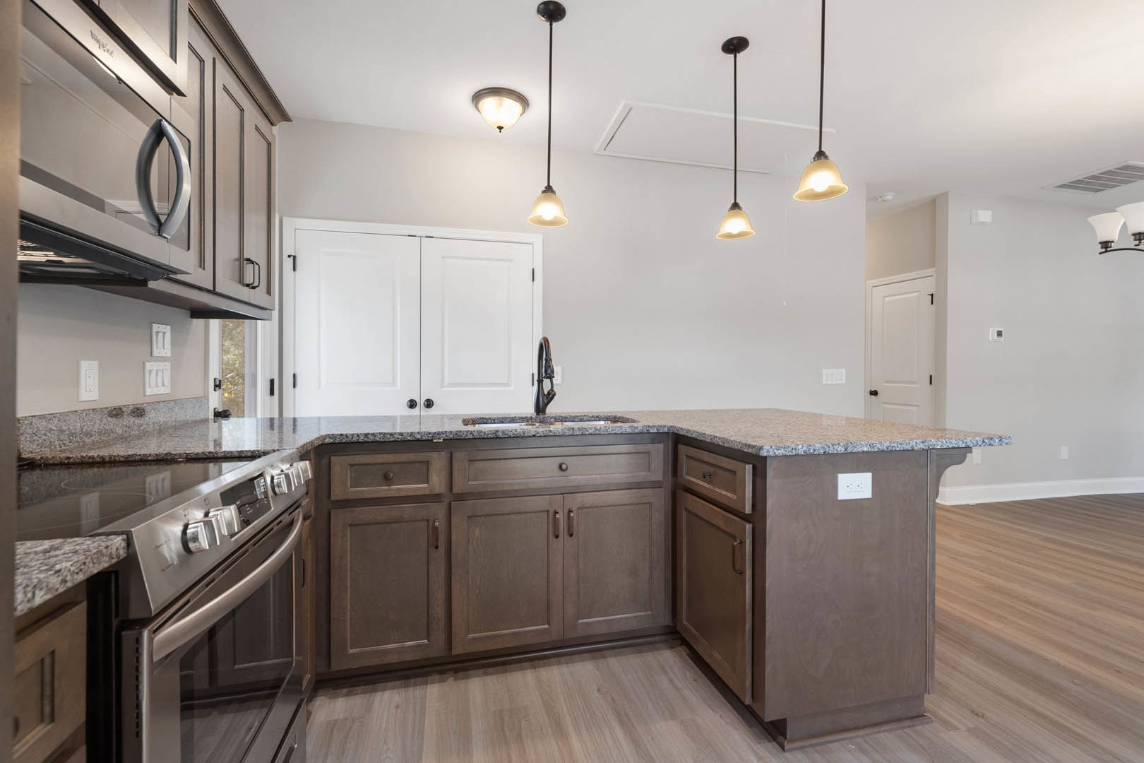 Marble countertop kitchen with white cabinets featuring black knobs, pendant light fixture hanging from ceiling, stainless steel appliances, and light wood flooring.