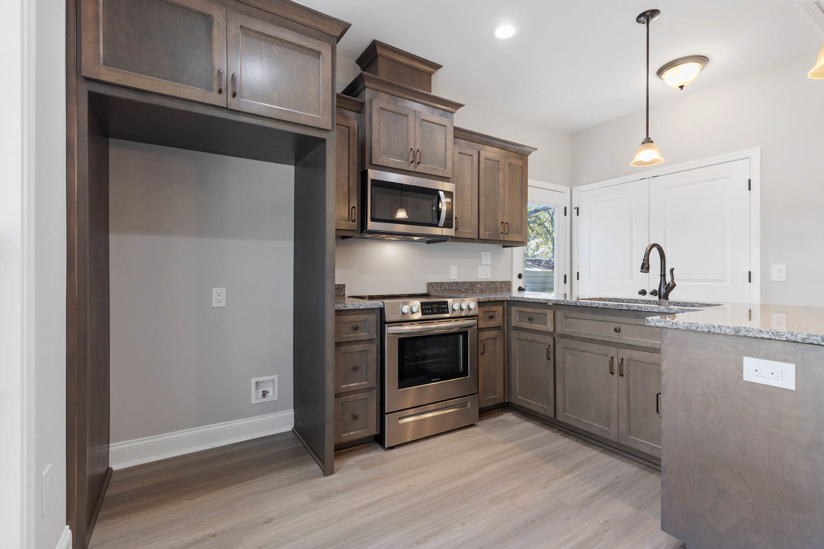 Kitchen with natural wood cabinets, stainless steel stove and oven, built-in microwave, stone countertops, pendant light fixture, and hardwood flooring