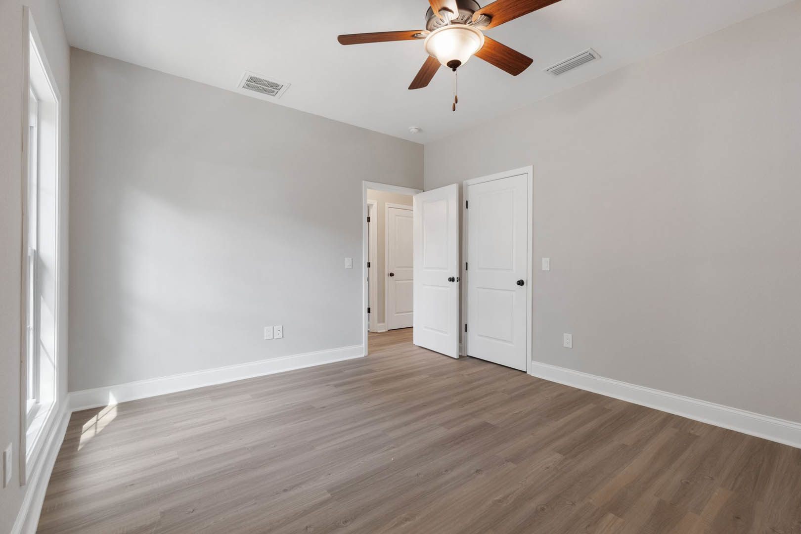 Ceiling fan with light and wooden blades mounted above wood flooring, white doors with black knobs, wall vent, and plaster walls