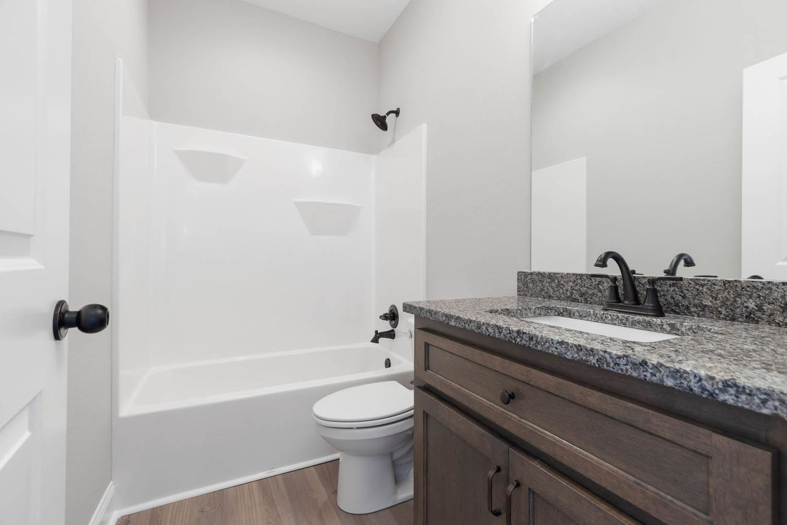 White tile bathroom featuring a marble countertop vanity with undermount sink, chrome faucet, modern toilet, black shower head mounted on a white wall, and brushed metal doorknob.