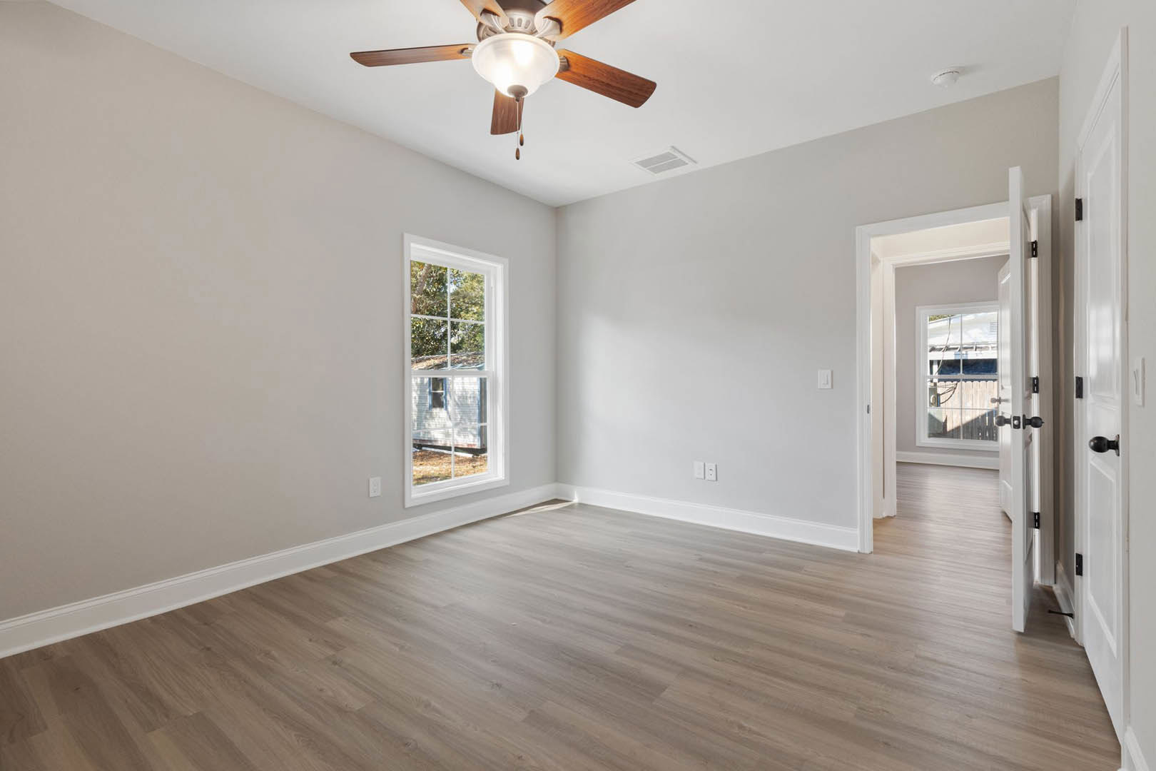 Ceiling fan with light fixture above hardwood floor, white-framed window overlooking trees, plaster walls, and neutral interior finishes