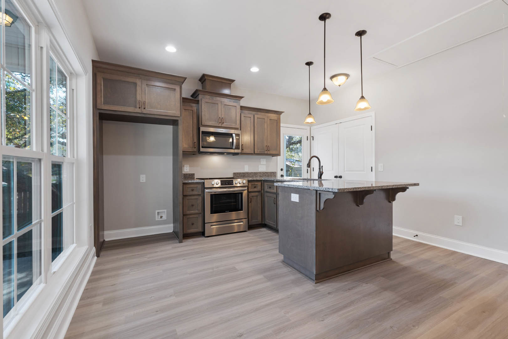 Kitchen with hardwood flooring, central island featuring granite countertops, white cabinetry, stainless steel stove, pendant light fixture, and wall-mounted light switch