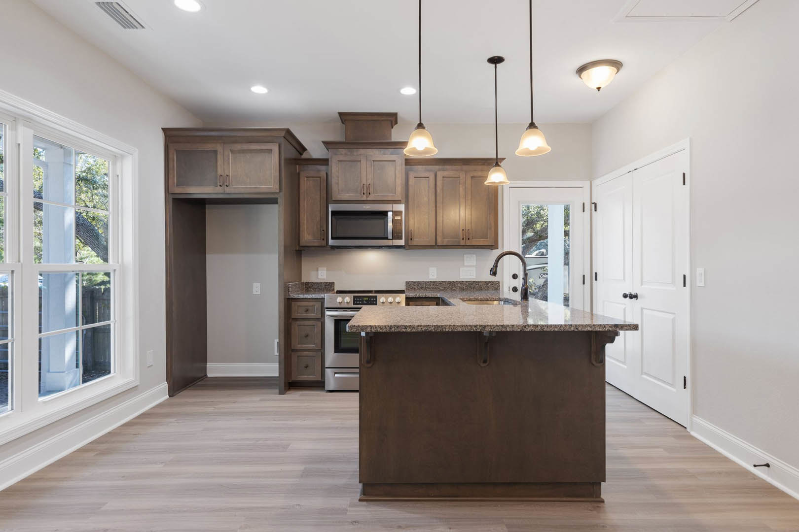 Modern kitchen featuring a central island with white cabinetry, stainless steel microwave with glass door, stone countertop with undermount sink, large window, black cabinet knobs