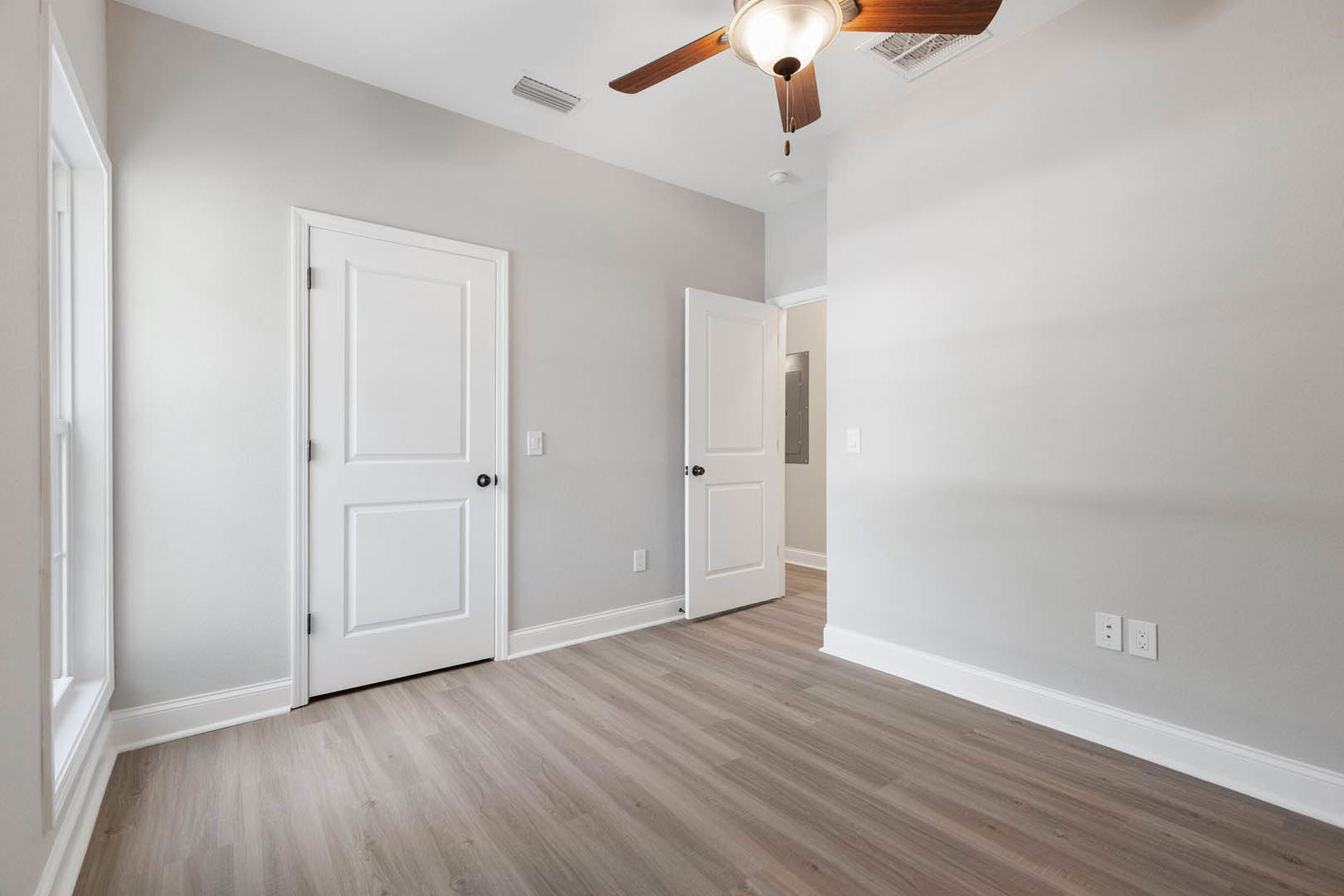 Room with wood flooring, two white doors with black knobs, light gray walls, and a ceiling fan with a light fixture and wooden blades