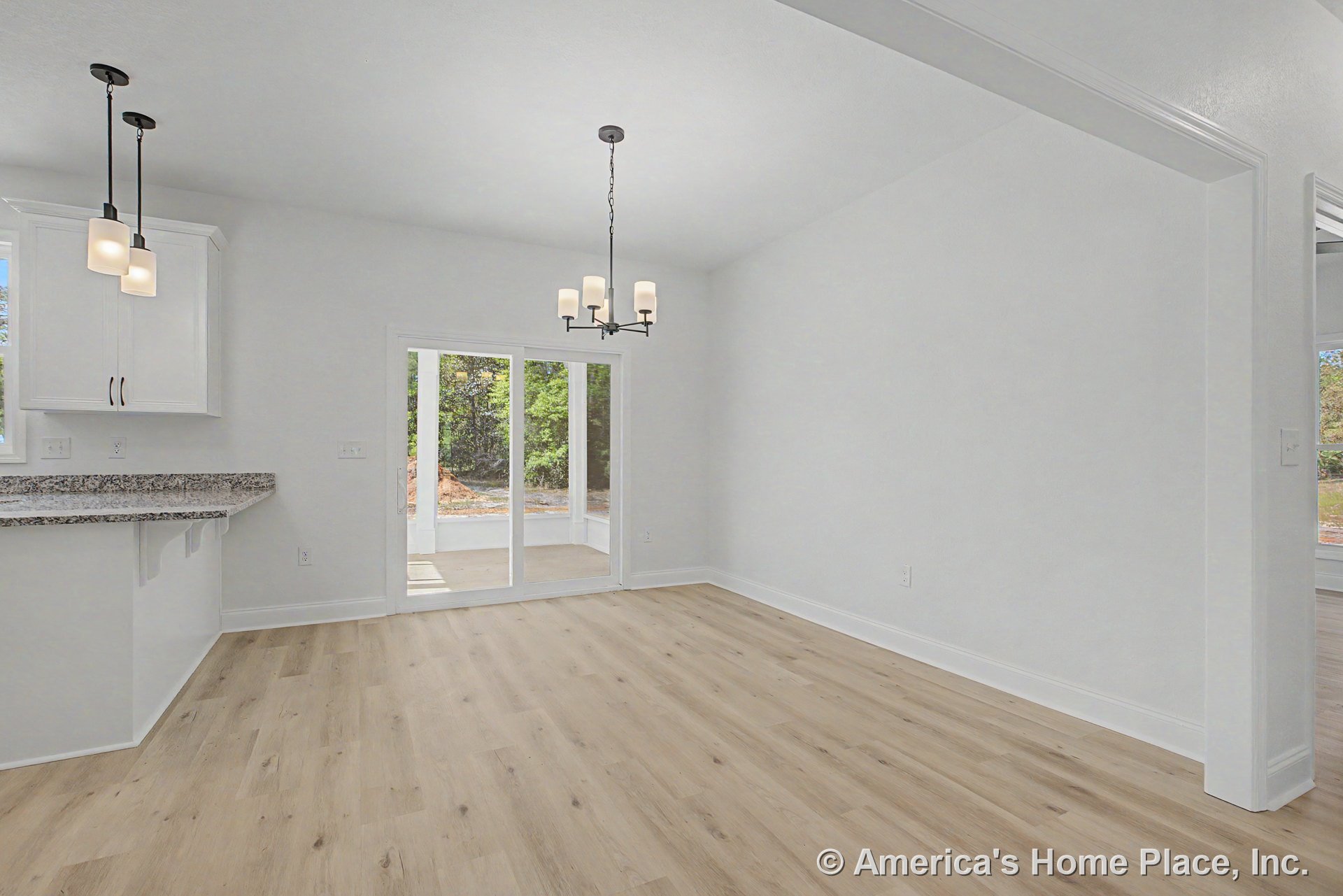 Dining area with light wood plank flooring, white trim and baseboards, modern chandelier, sliding glass doors opening to a covered patio, granite kitchen countertop, and white