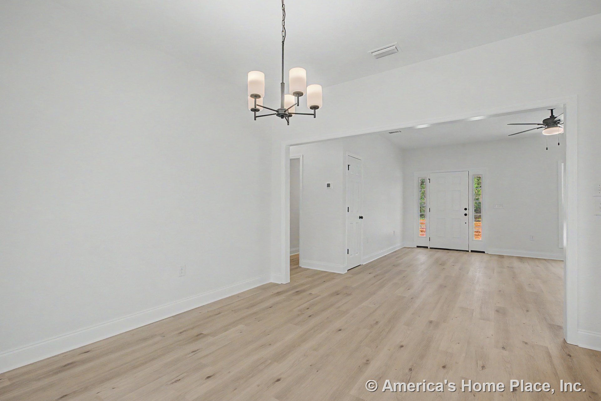 Open entryway and dining area with light wood plank flooring, white interior doors, large baseboards, modern chandelier, ceiling fan with built-in light, and white walls in an open