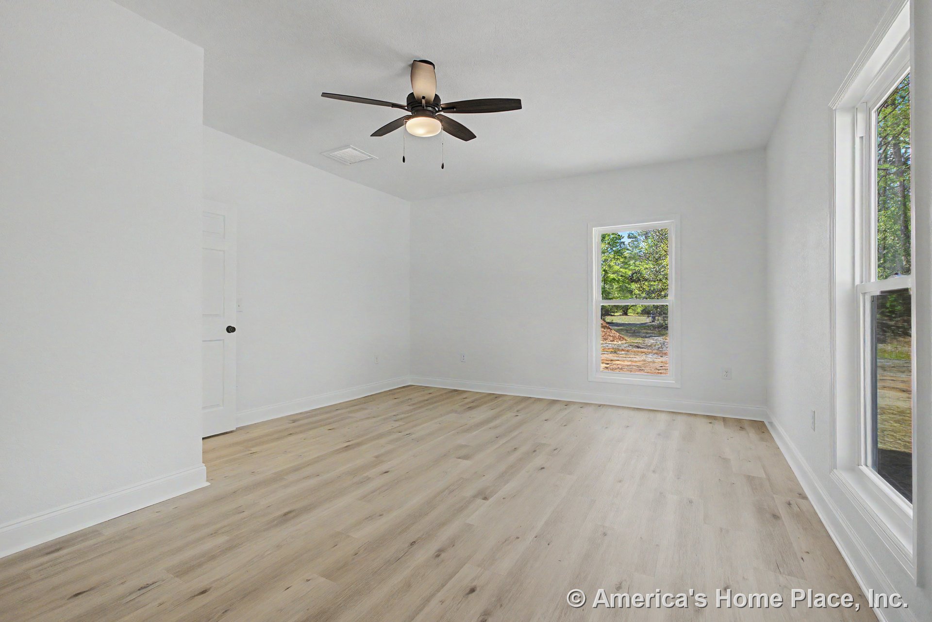Bedroom with light wood-look flooring, white painted walls, ceiling fan with integrated light, double-hung windows, white trim and baseboards, and paneled interior door.