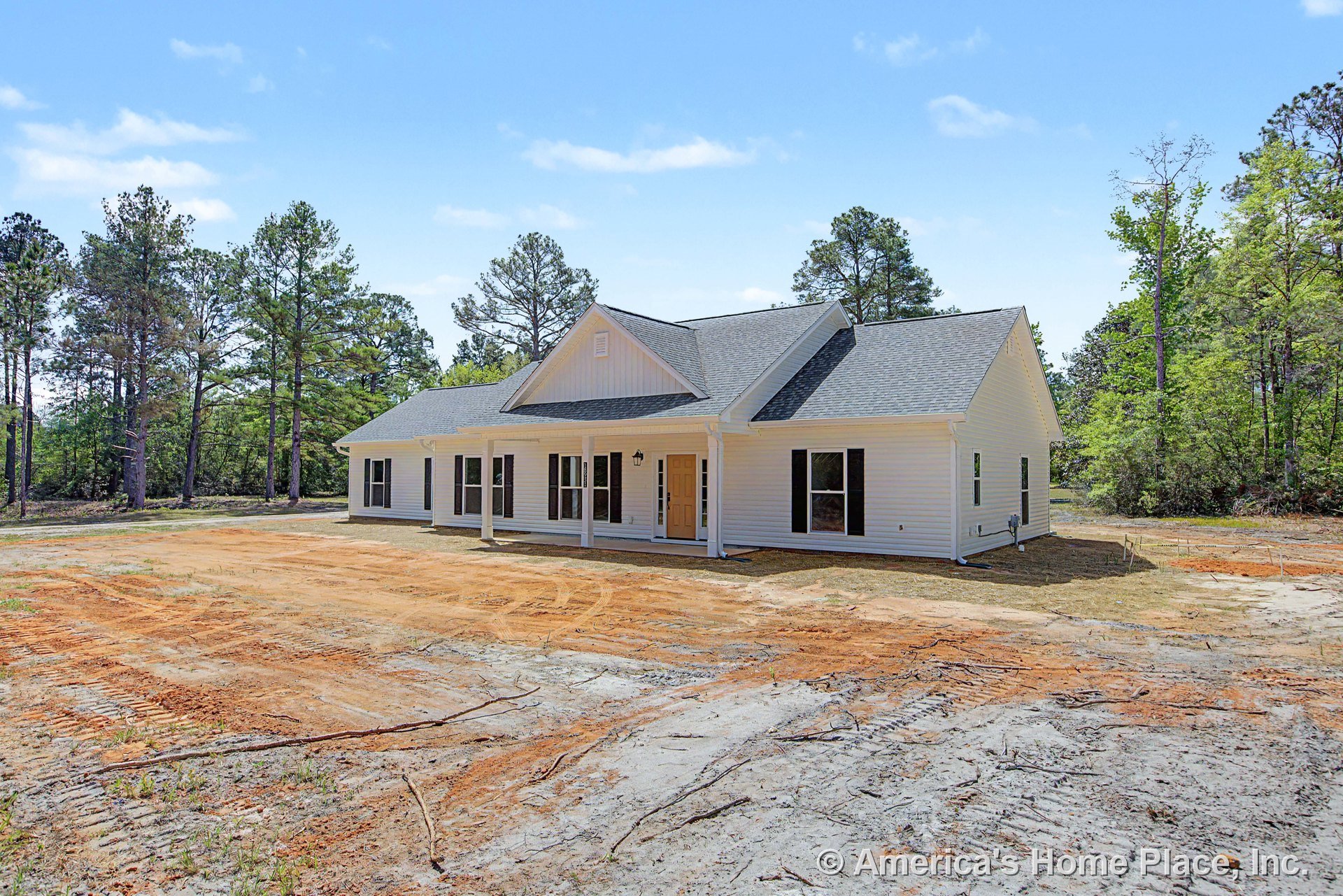 Covered front porch with white columns, yellow front door, multiple large windows, white siding exterior, gable roof, single-story layout, surrounded by wooded lot.