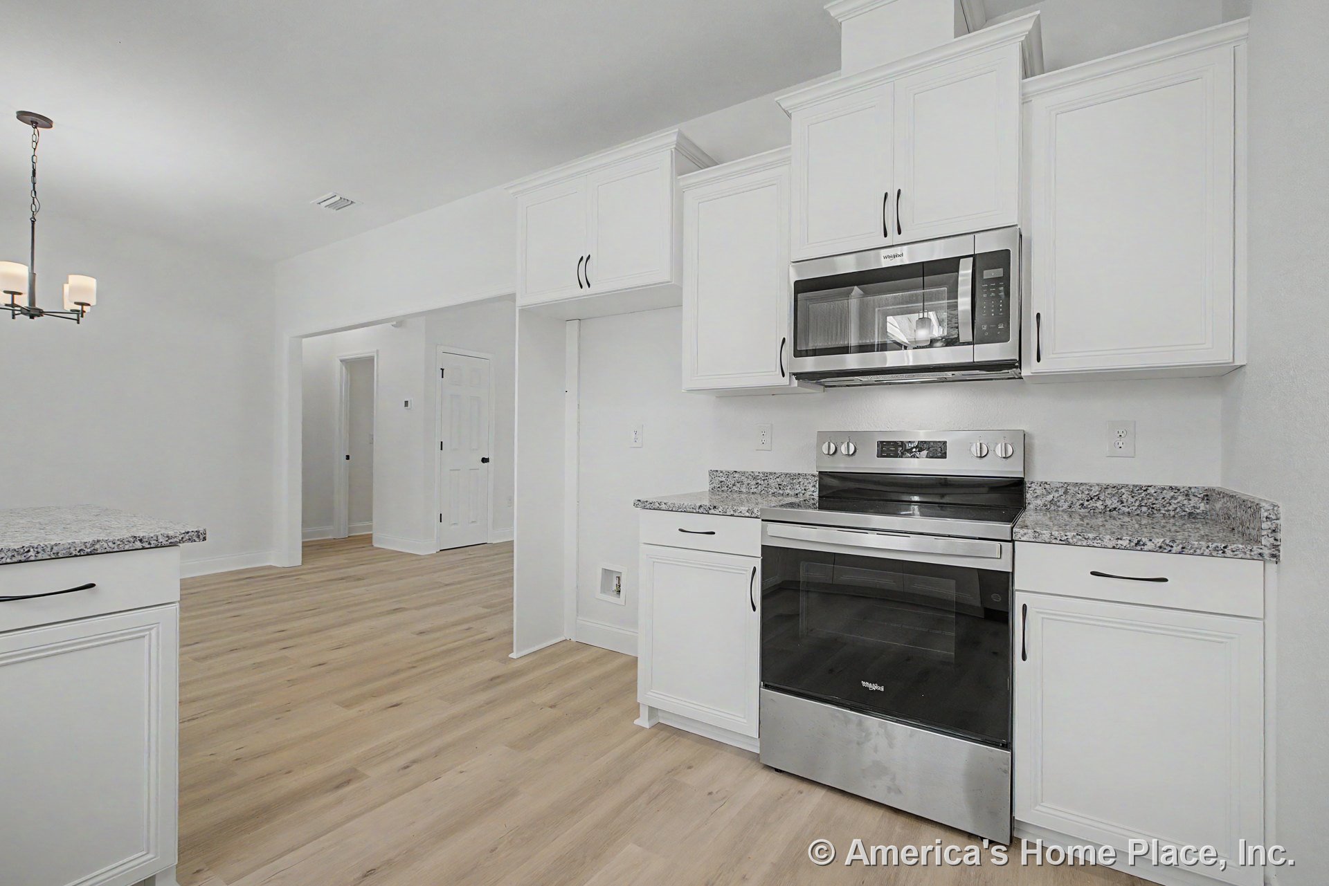 White upper and lower kitchen cabinets with granite countertops, stainless steel oven and microwave, light wood plank flooring, built-in ceiling light fixture, trimmed doorways and