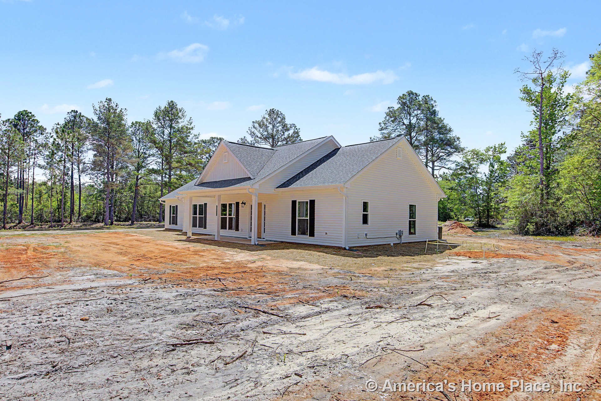 Covered front porch with white columns, white vinyl siding, black window shutters, gable roof, double front doors, exterior lighting fixture, and crisp trim in a rural new