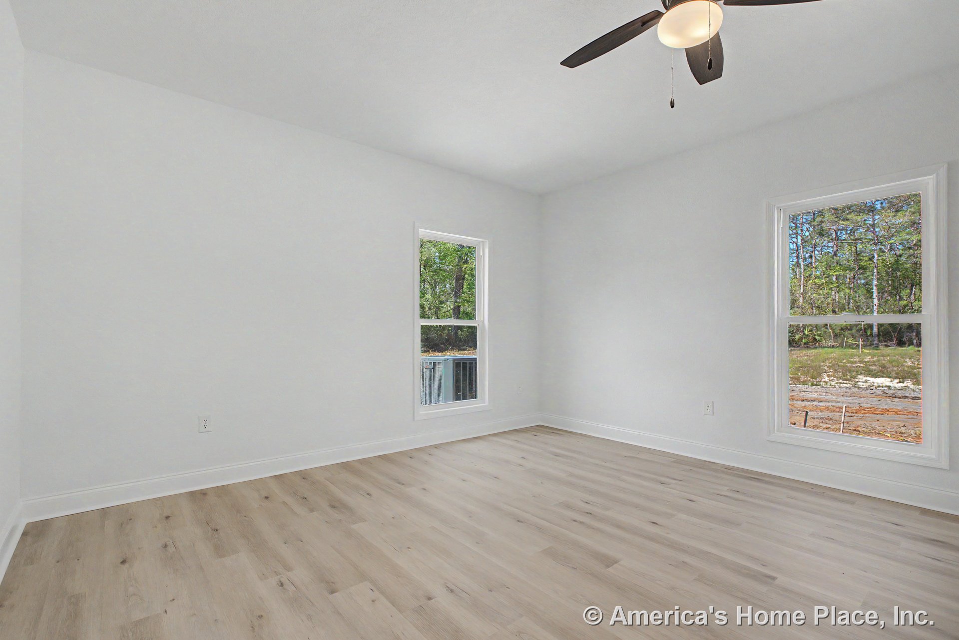 Bedroom with light wood-look flooring, white painted walls, two large windows, ceiling fan with integrated light, white baseboards, and flat ceiling.