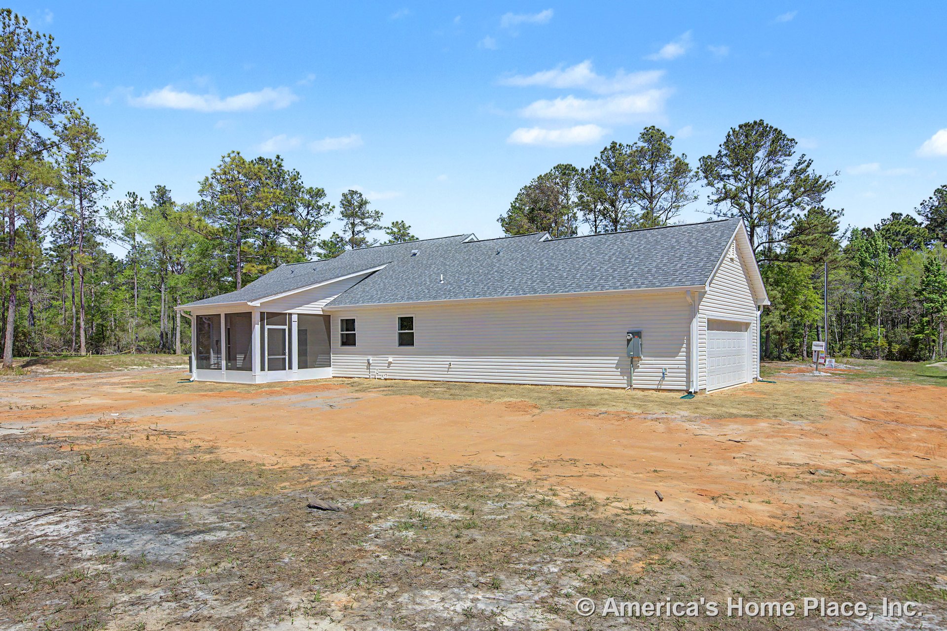 Single-story home with light vinyl siding, asphalt shingle roof, attached two-car garage, screened porch, multiple rectangular windows, and wooded lot backdrop.
