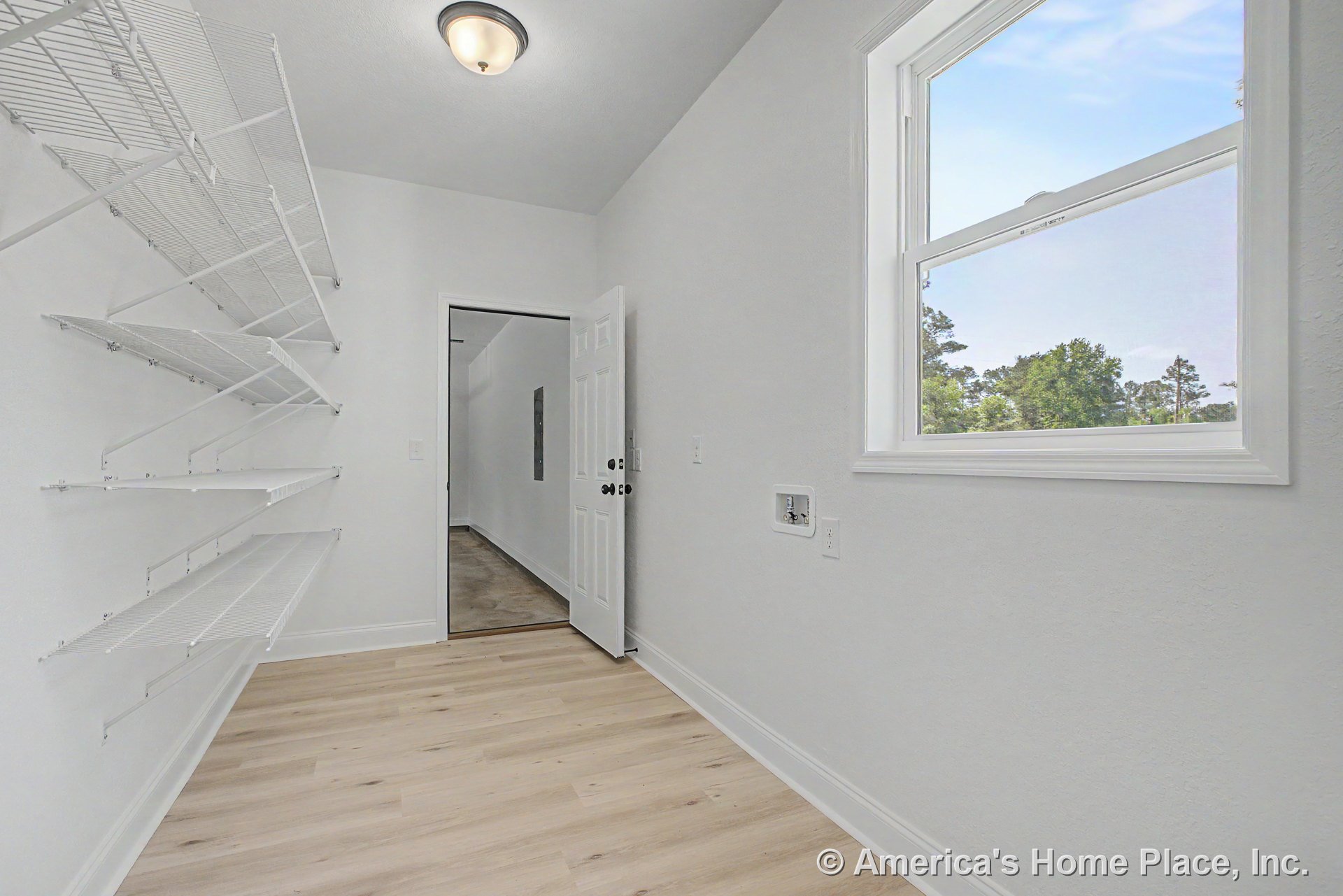 Laundry room with wall-mounted wire shelving, large double-hung window, light wood plank flooring, white painted trim, ceiling-mounted light fixture, and washer and dryer hookups.