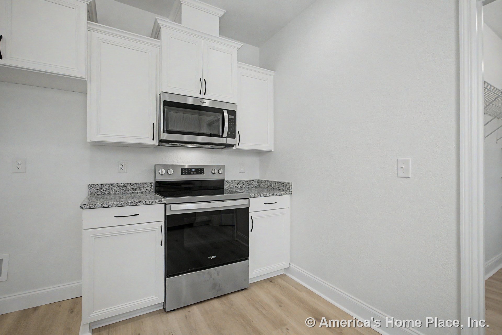White upper and lower cabinets with granite countertops and matching backsplash, stainless steel electric range with built-in microwave above, light wood flooring, and white