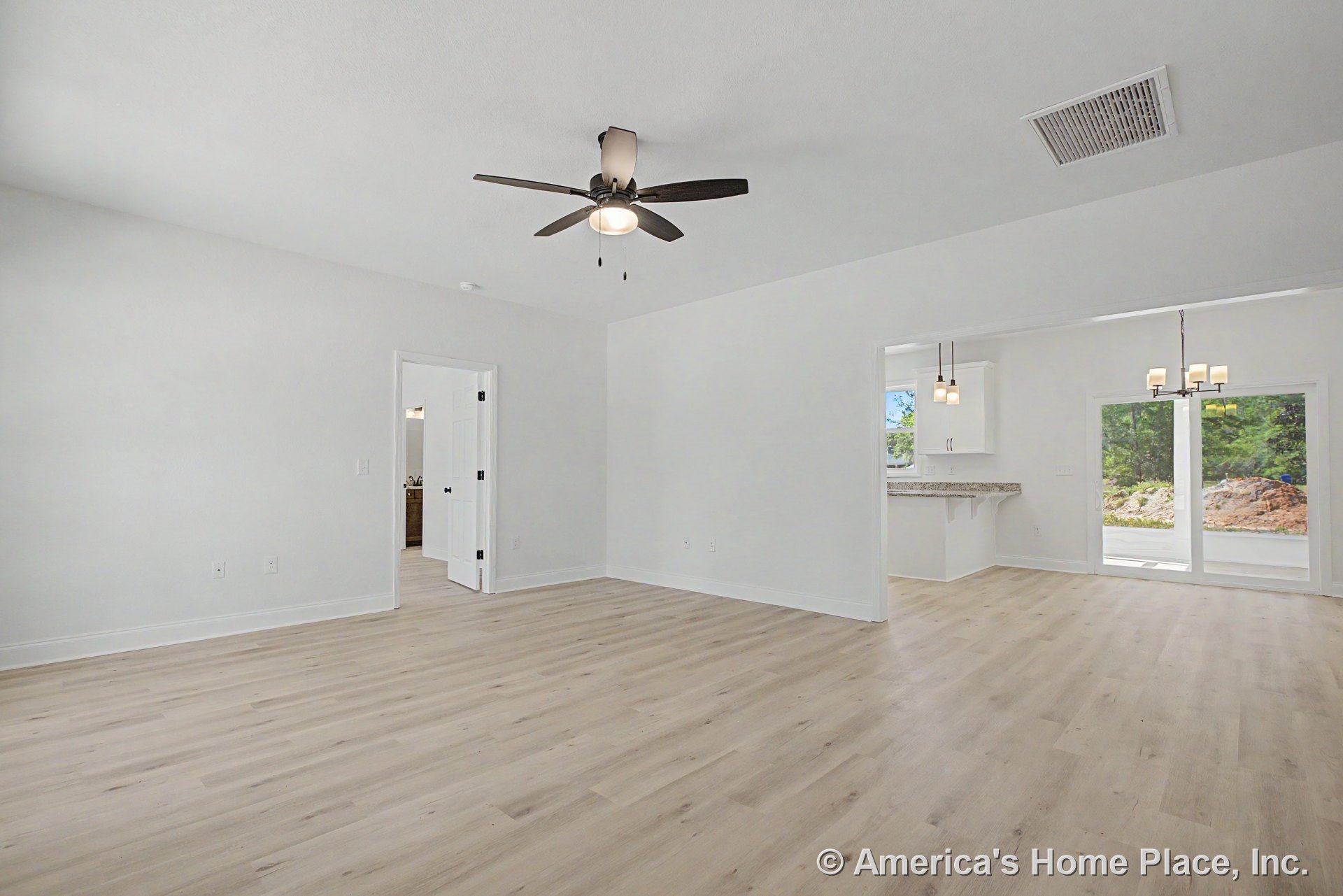 Light wood plank flooring and white trim in a living area with ceiling fan, open layout connecting to kitchen with white cabinetry and granite countertops, dining space, sliding