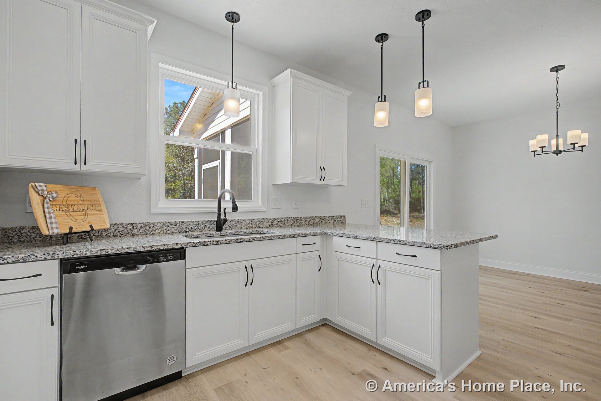 White shaker cabinets with brushed hardware, granite countertops, stainless steel dishwasher, undermount sink beneath double window, pendant lights above island, light wood