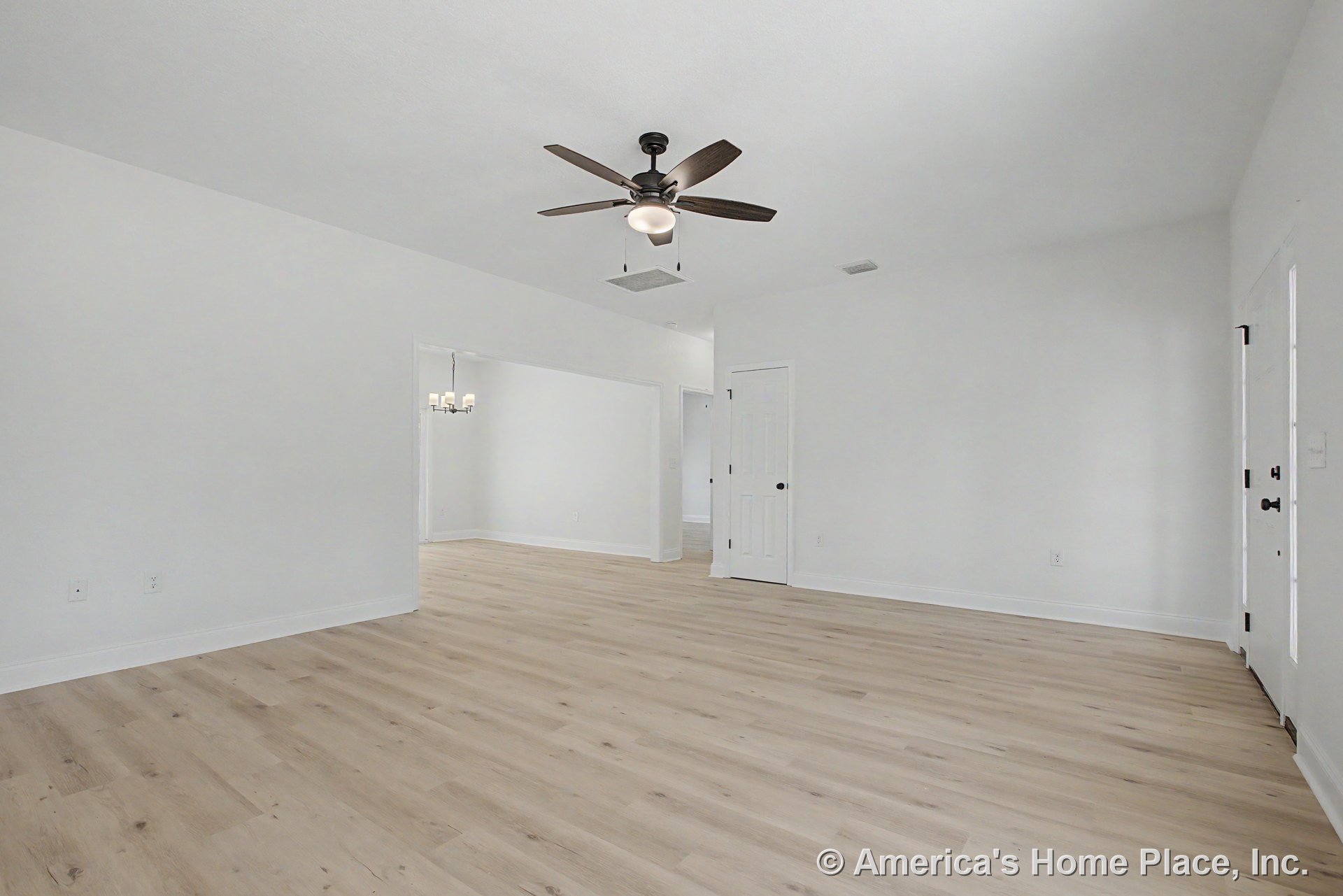 Light wood plank flooring and white painted trim in living area, ceiling fan with integrated light overhead, interior door with black hardware, open layout connecting to dining