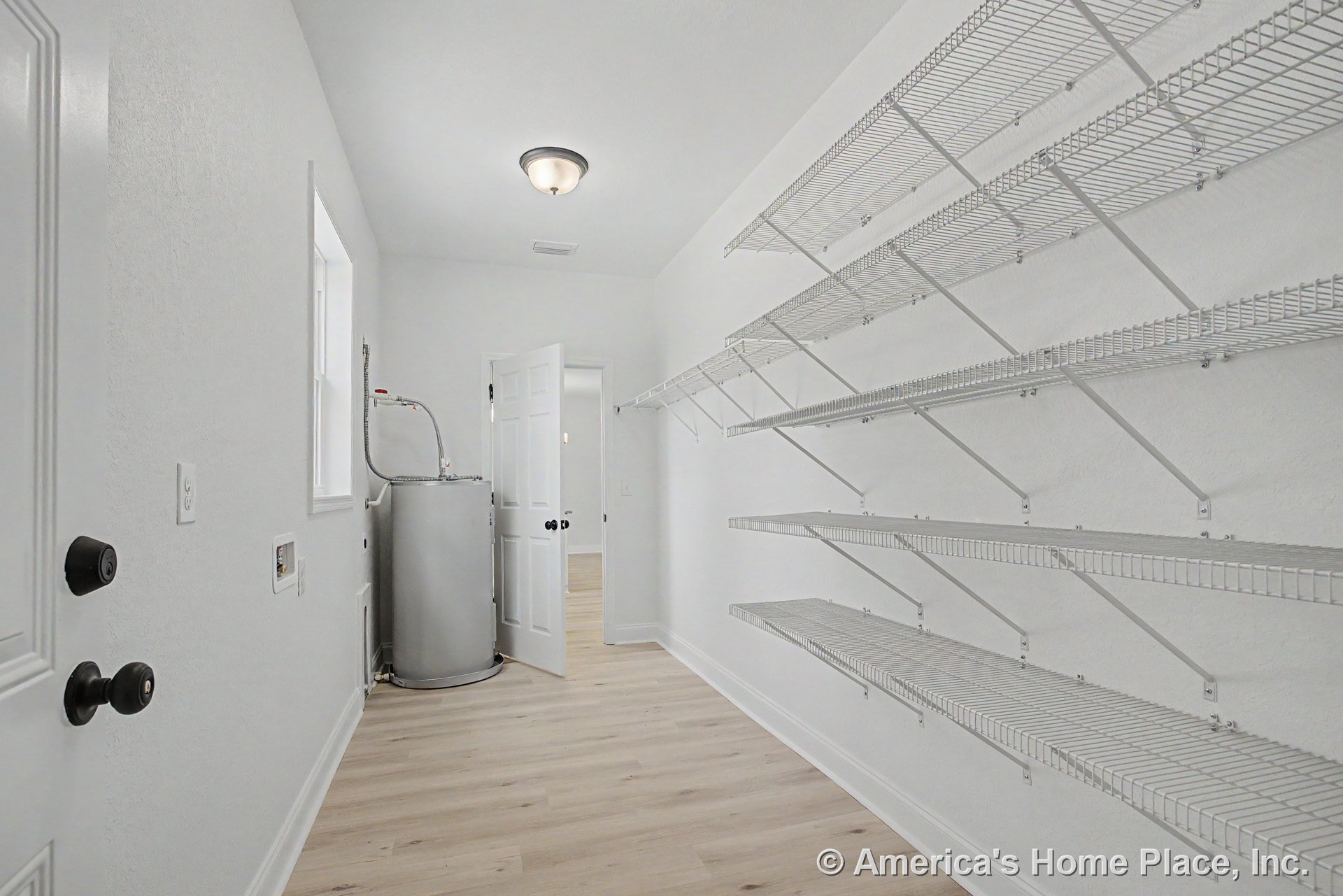 Laundry room with multiple wall-mounted wire shelves, water heater, white painted walls, light wood flooring, flush mount ceiling light, laundry hookups, door, and window.