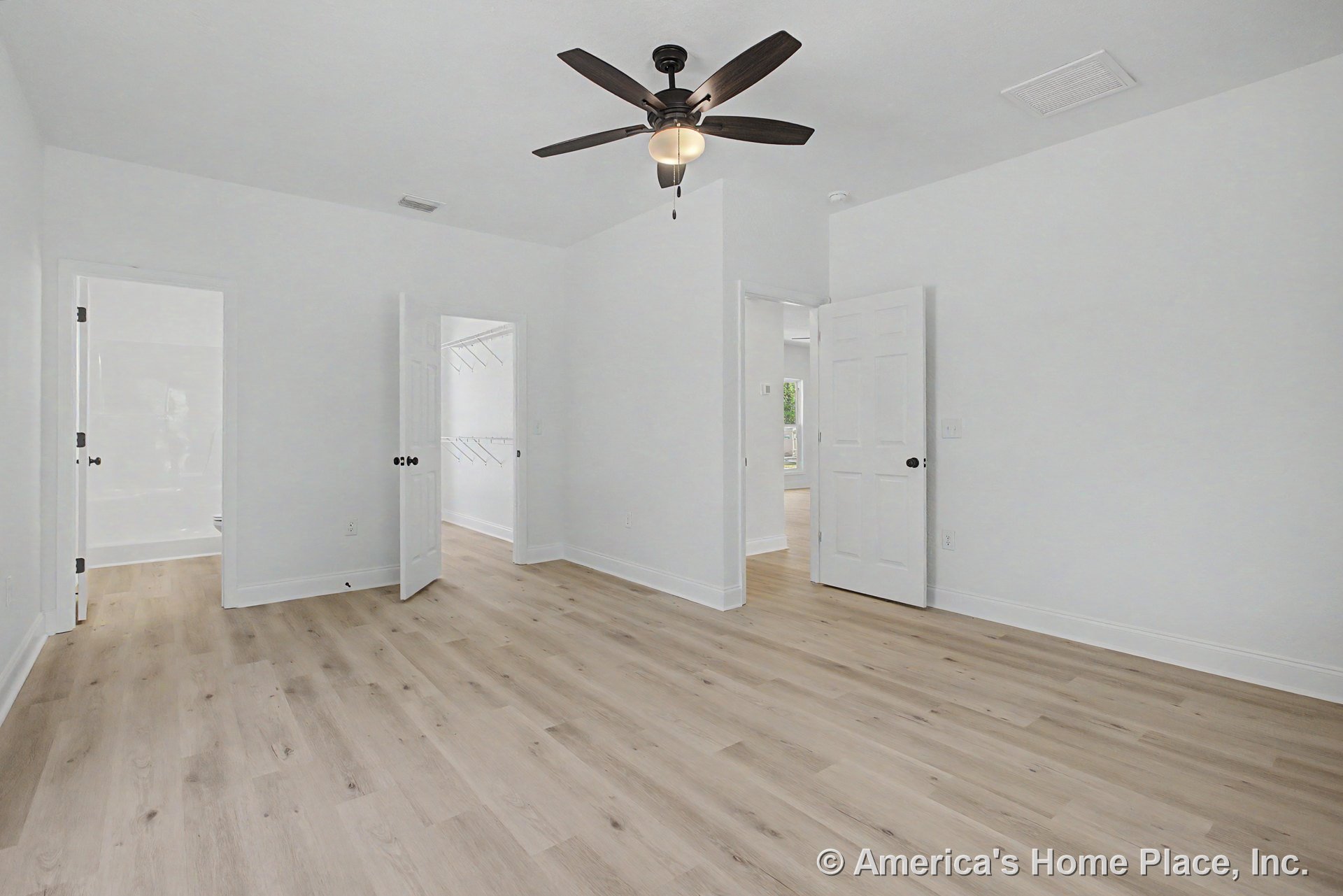 Bedroom with light wood plank flooring, white walls and baseboard trim, ceiling fan with integrated lighting, multiple paneled doors, walk-in closet featuring wire shelving, and