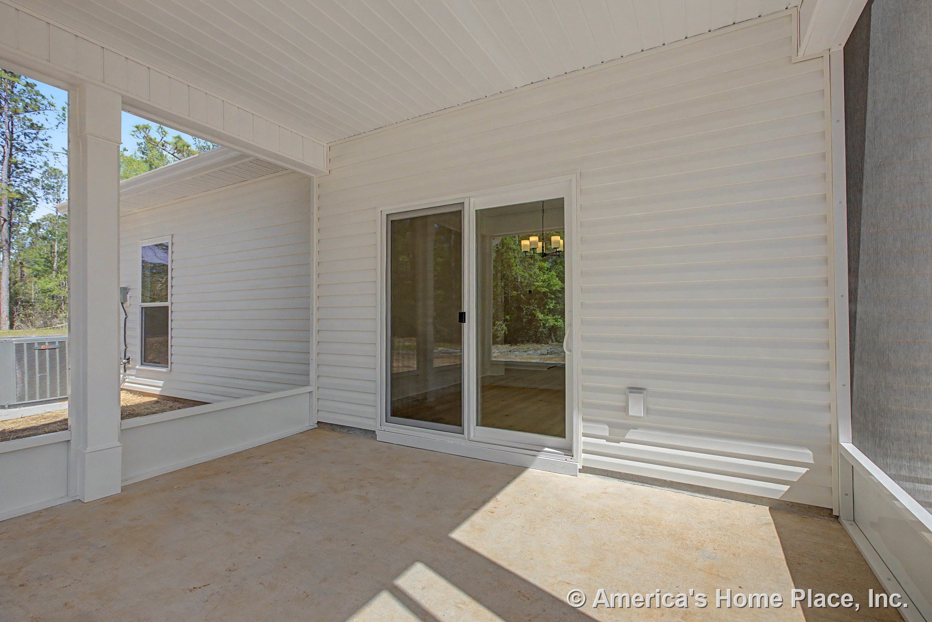 Covered porch with white vinyl siding walls, concrete floor, sliding glass door, trimmed window, built-in railing, and ceiling-mounted lighting fixture.