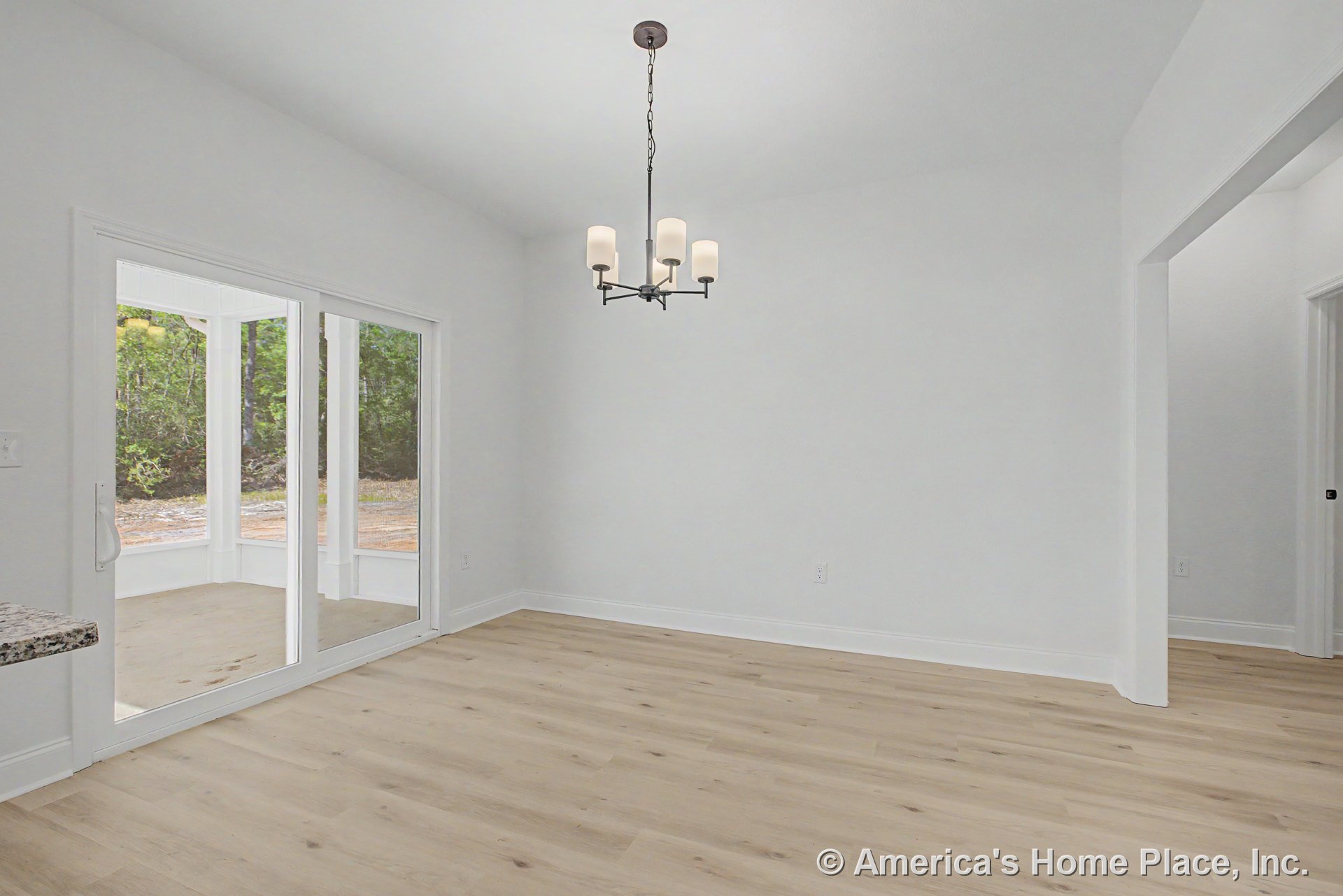 Dining area with light wood plank flooring, white walls and trim, modern ceiling chandelier, sliding glass doors opening to a covered porch, and open doorway connecting to adjacent