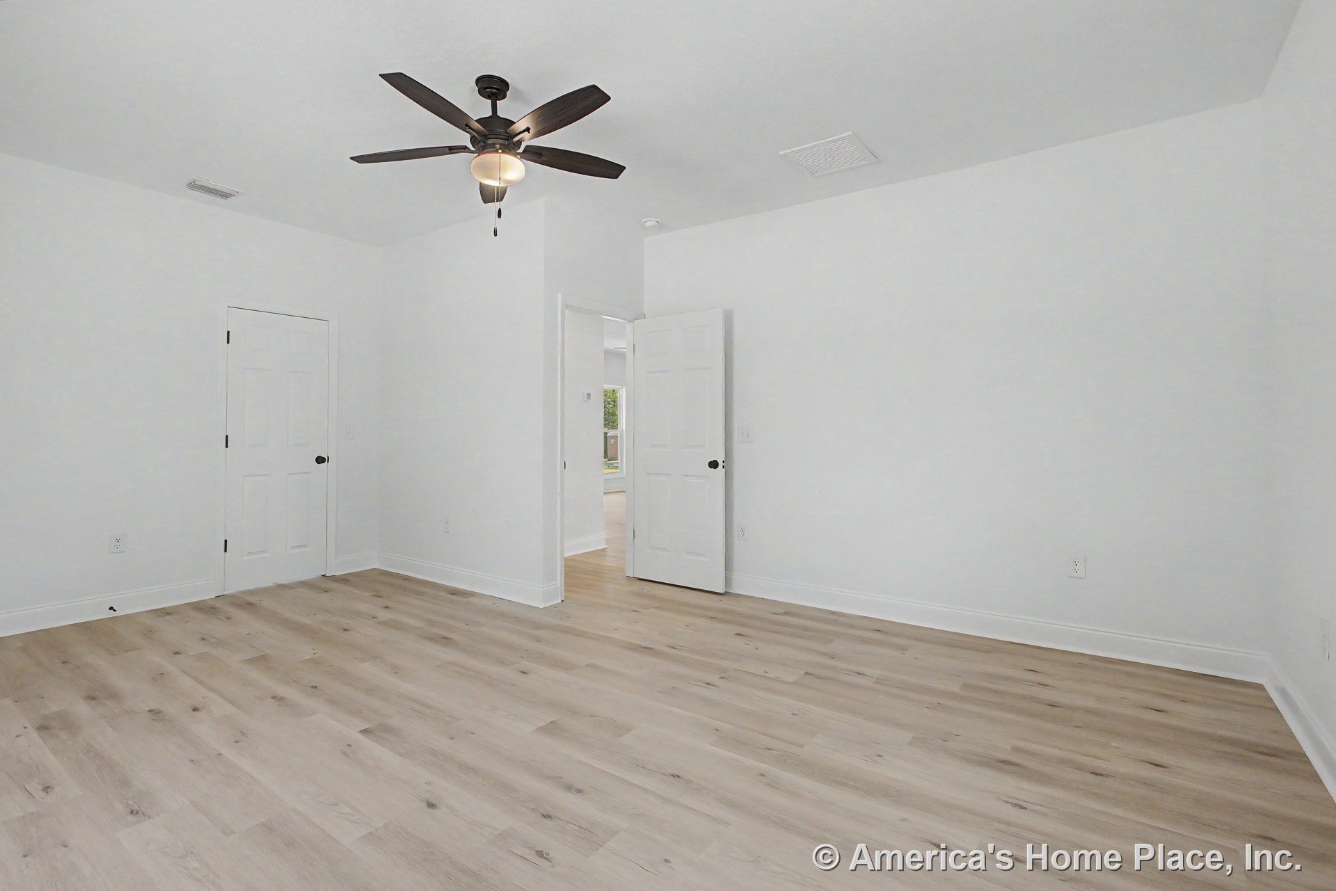 Bedroom with light wood plank flooring, smooth white walls and ceiling, white baseboards, paneled doors, and ceiling fan with integrated light fixture.