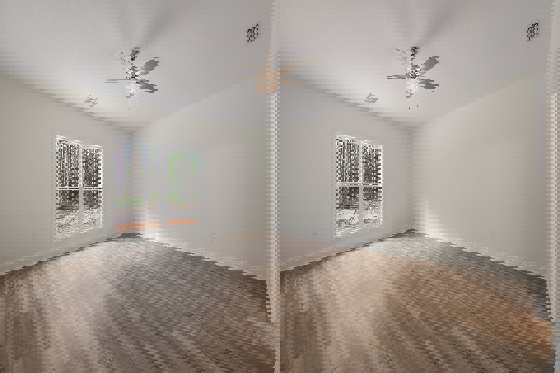 Bedroom with wood flooring, white plaster walls, ceiling fan with light fixture, large window overlooking trees.