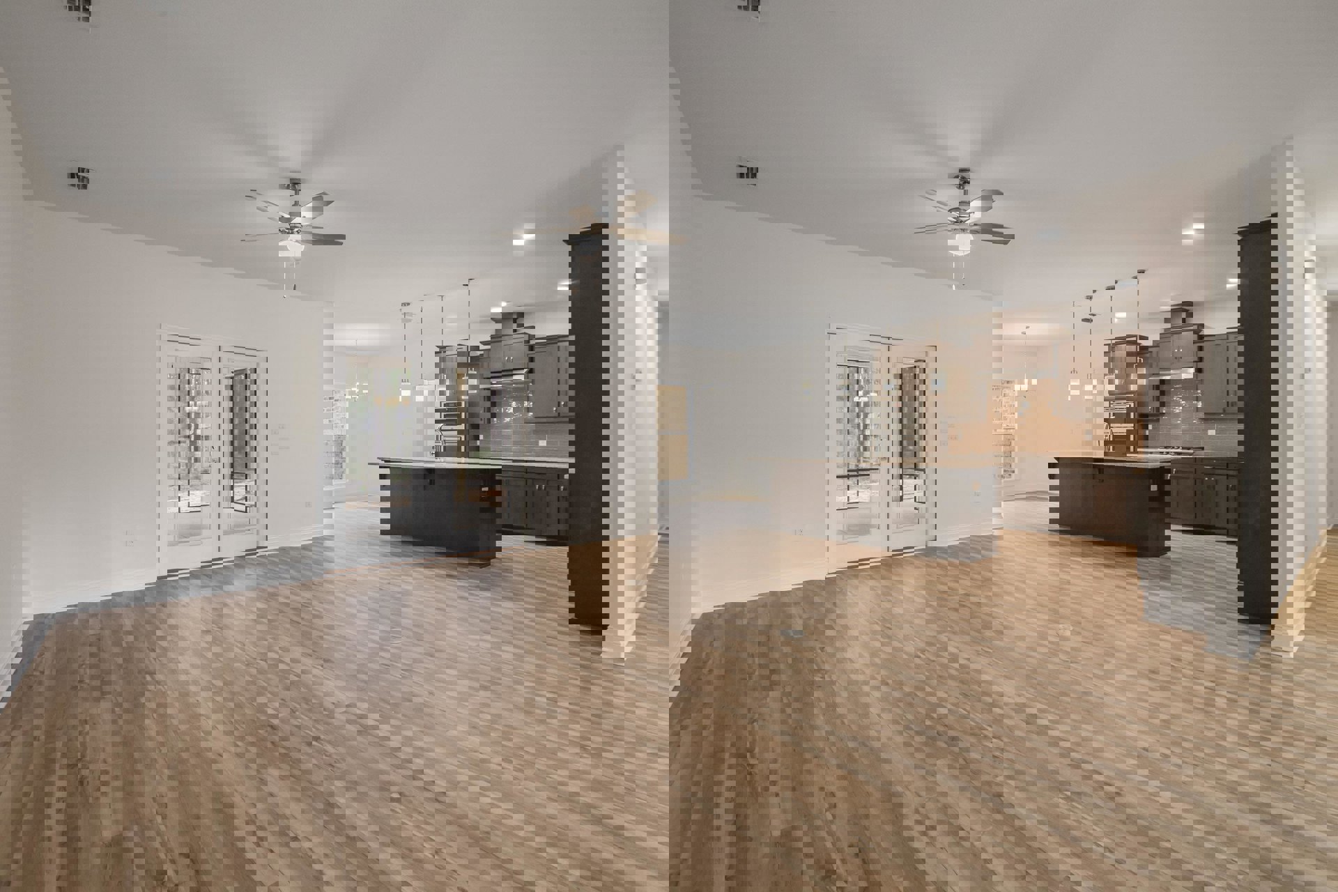 Spacious open-plan kitchen with central island, hardwood flooring, ceiling fan with light, white double doors with mirrored panels, glass door and window overlooking forest scenery