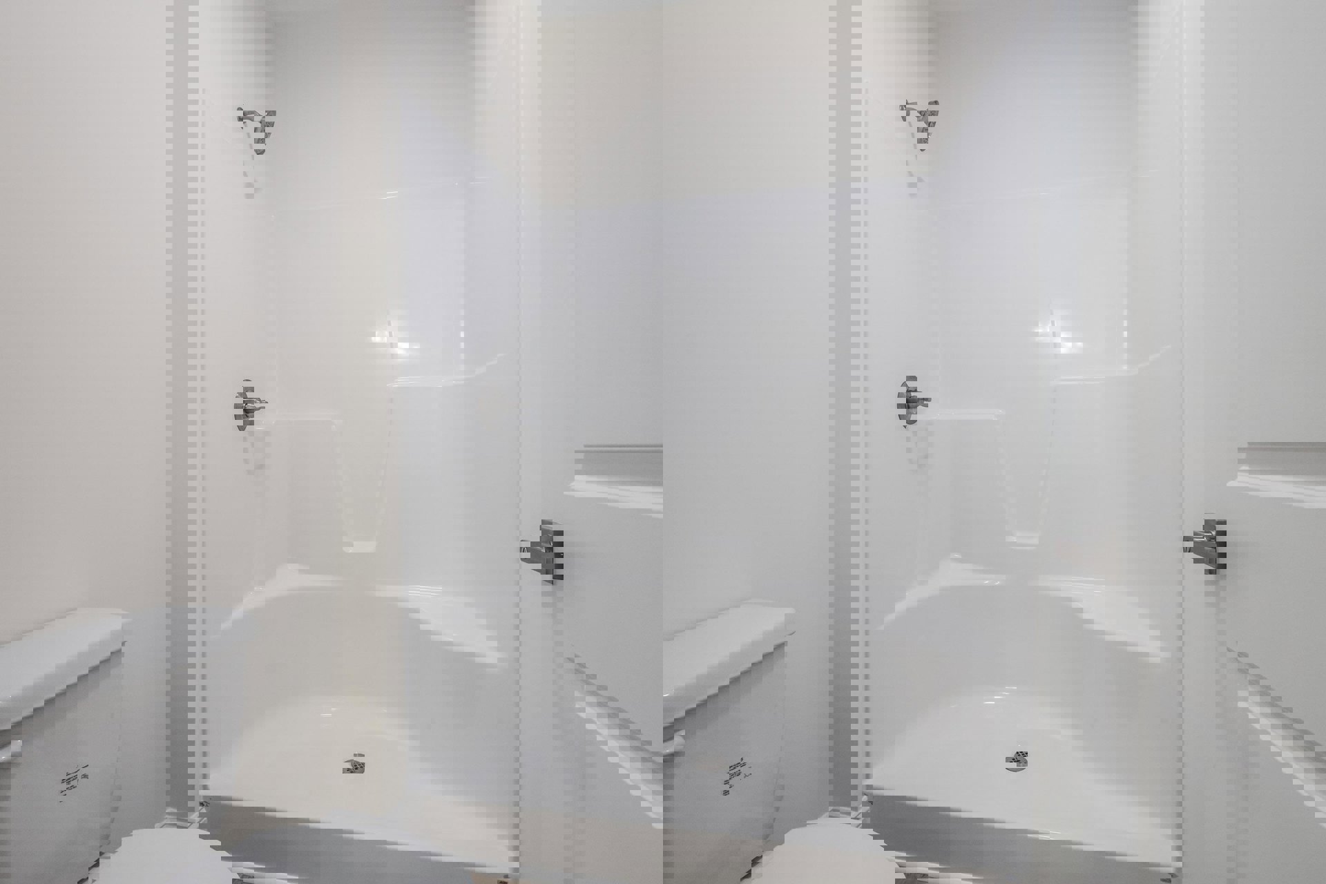 White tiled shower with chrome showerhead and metal knob, adjacent to white bathtub, toilet tank, and close-up door handle.