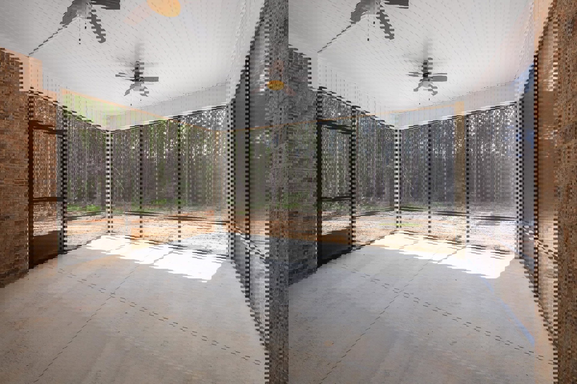 Ceiling fan with light fixture on white ceiling, large window with view of trees, glass wall, close-up of exposed brick wall, hardwood floor