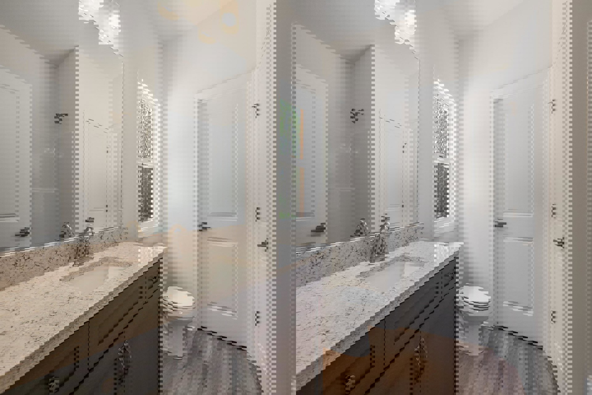 Marble countertop with undermount sink, white toilet, tile flooring, window overlooking trees, white door with metal handle