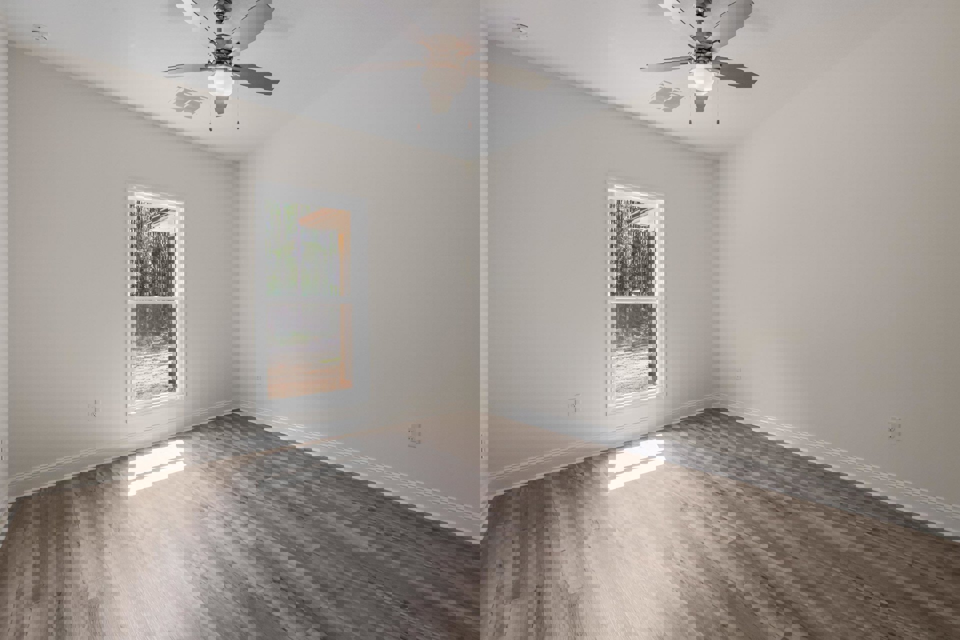 Ceiling fan with light fixture on white ceiling, large window with sheer white curtain overlooking trees, wood laminate flooring, white walls, and white air vent