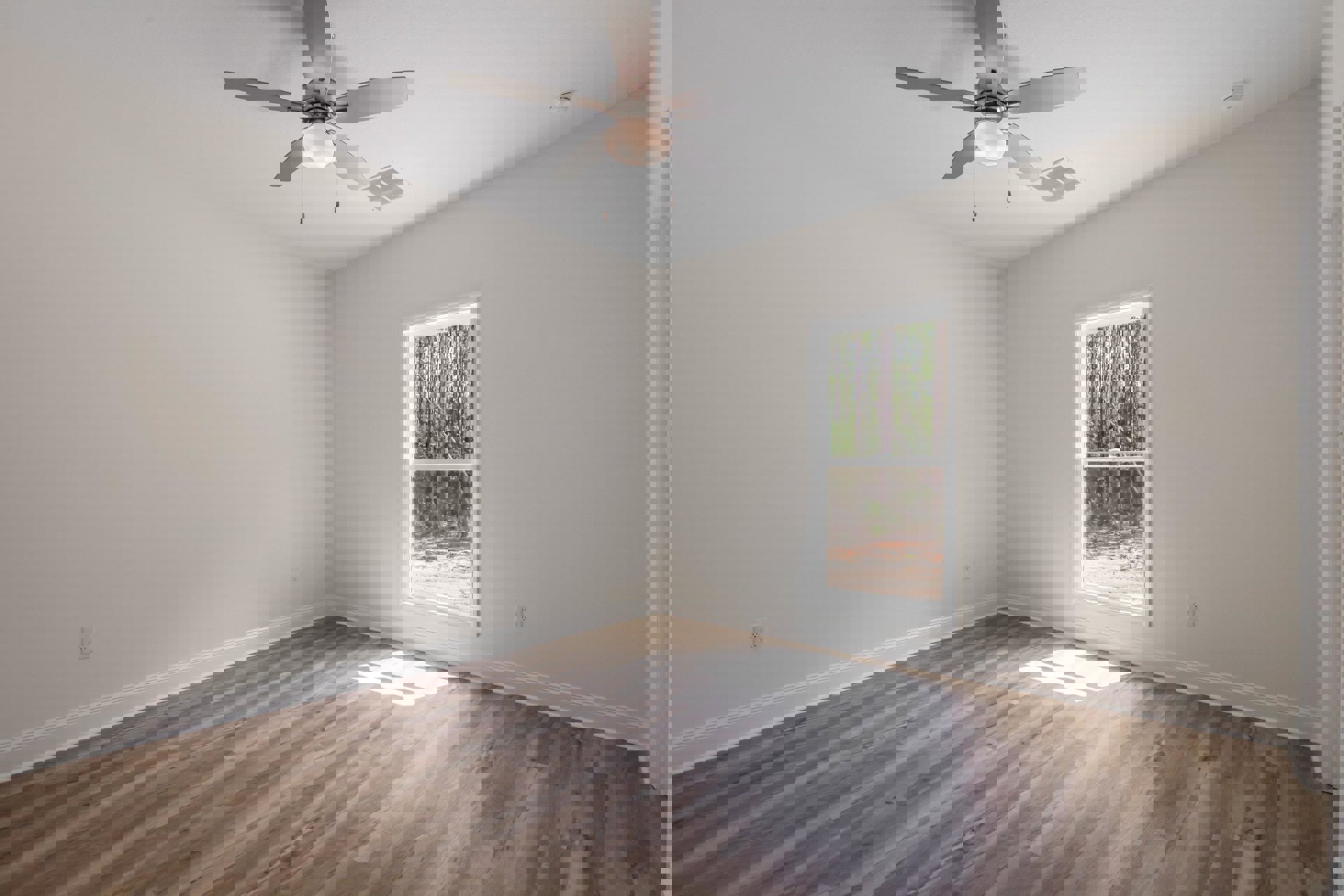 Ceiling fan with light fixture above wood flooring, sunlight streaming through window with view of green trees, white walls and plaster ceiling.