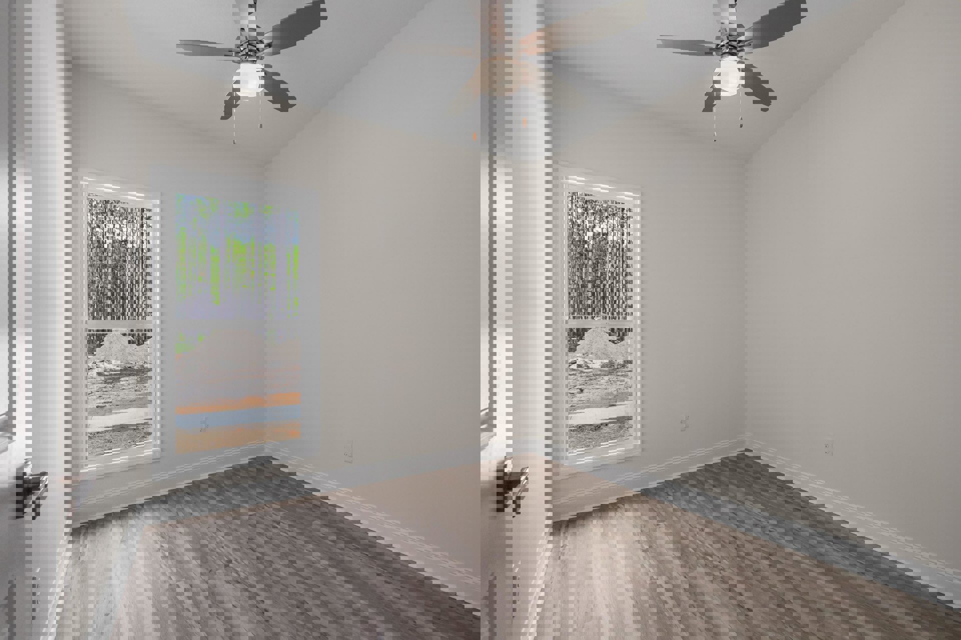 Ceiling fan with light fixture mounted above wood flooring and white trim, large window overlooking pile of sand and trees, scattered dirt and debris near window