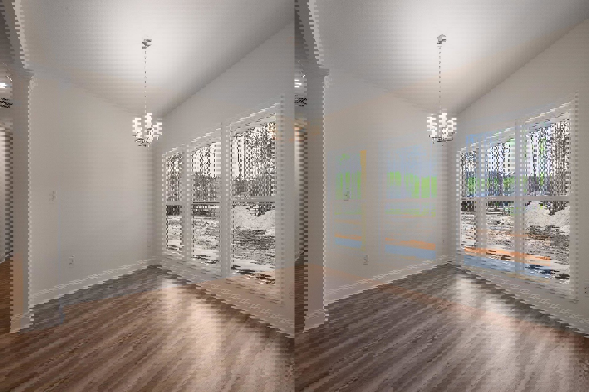 Chandelier hanging from white ceiling above wood flooring, large windows with views of trees, plaster walls